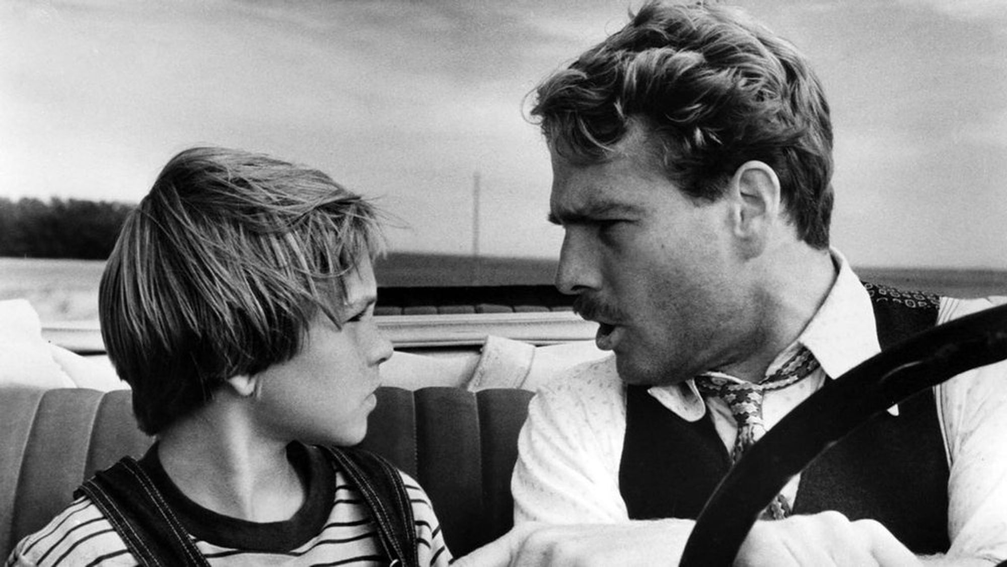 Bilde fra filmen Paper Moon: en mann skjeller ut en ung gutt mens de sitter i frontsetet av en cabriolet bil.