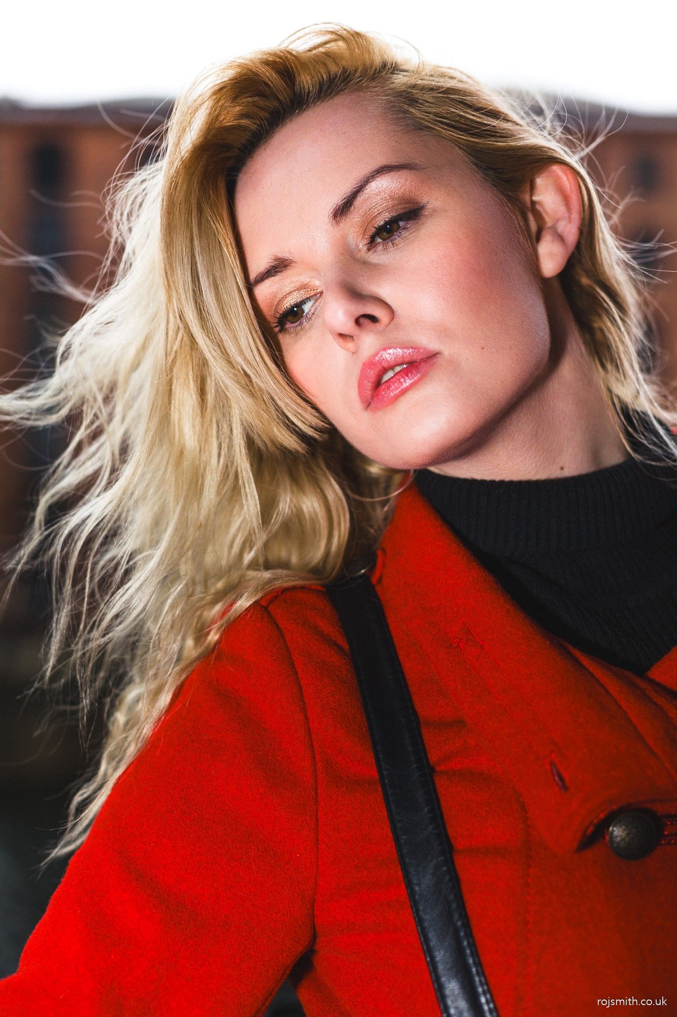 A woman with blonde hair, bright red coat and black jumper.