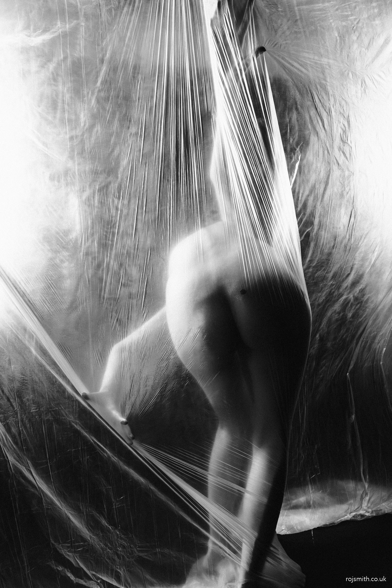 A nude woman appears behind a clear plastic sheet.