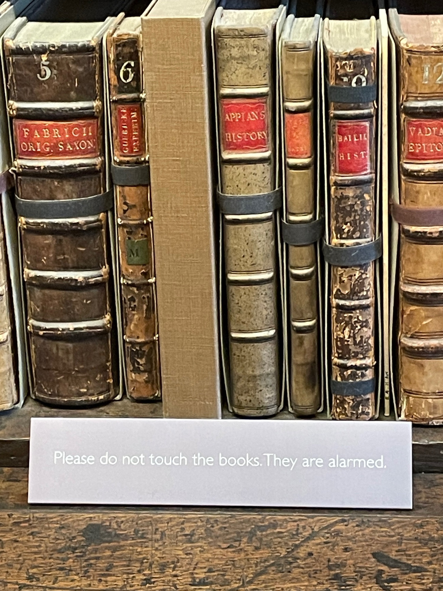 A shelf with very old books and a sign that reads. Please do not touch the books. They are alarmed.