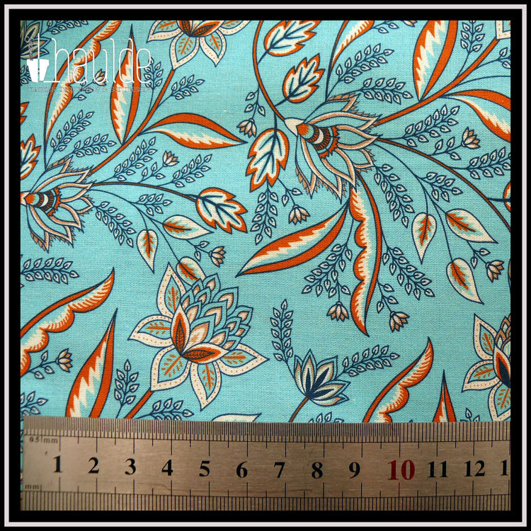 popeline fond bleu ciel clair avec des motifs floraux et végétaux de style indien, à dominante blanche et orange Une règle graduée indique que les motifs font environ 5 cm de large pour les fleurs, 7-8 cm pour les feuilles très allongées