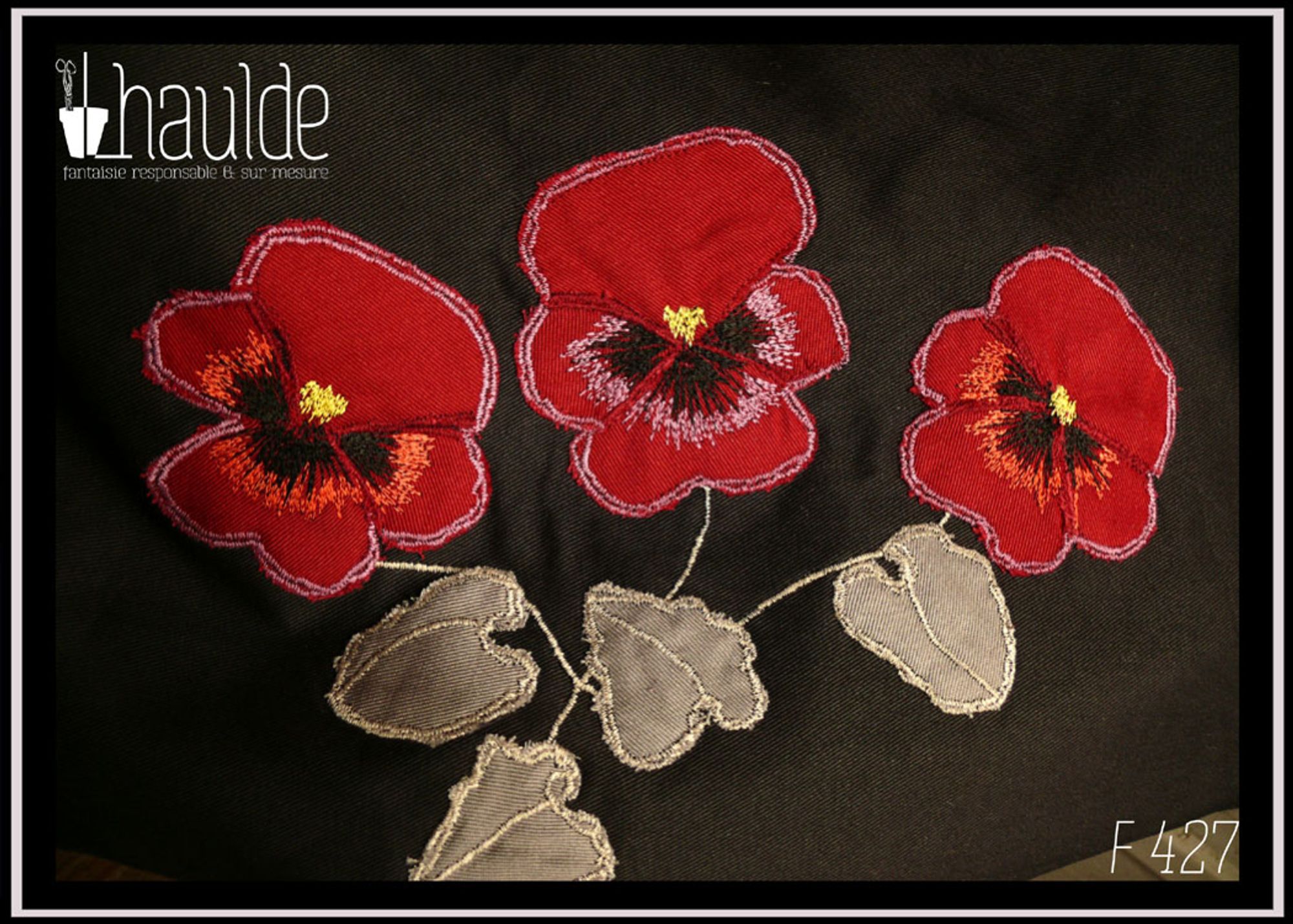 Sac en sergé noir, grand format horizontal à bandoulière, avec des appliqués en forme de pensées rouges avec leurs feuilles. Le centre des fleurs, les contours et les tiges sont brodés à la machine Vue de détail de la broderie