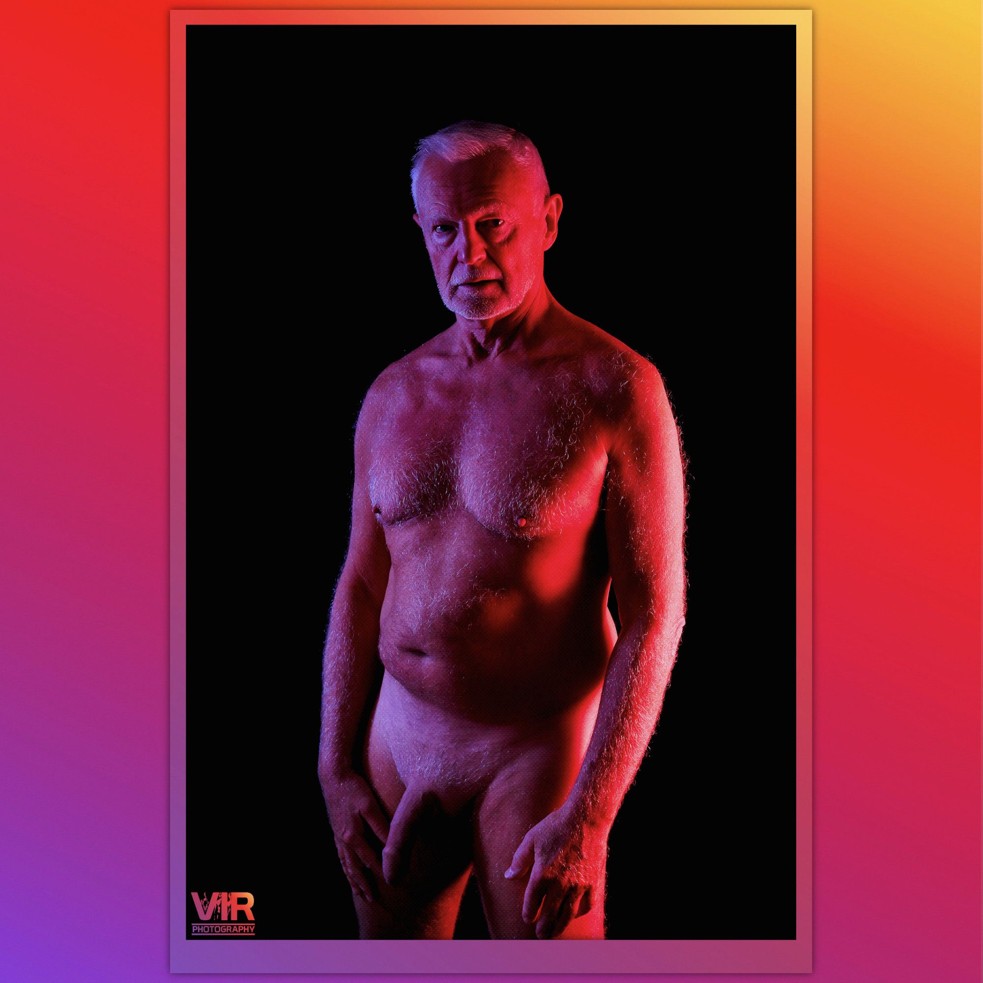 Image of a nude mature male model. The model is shot under colour gel lighting of red to the models left and blue to the right.