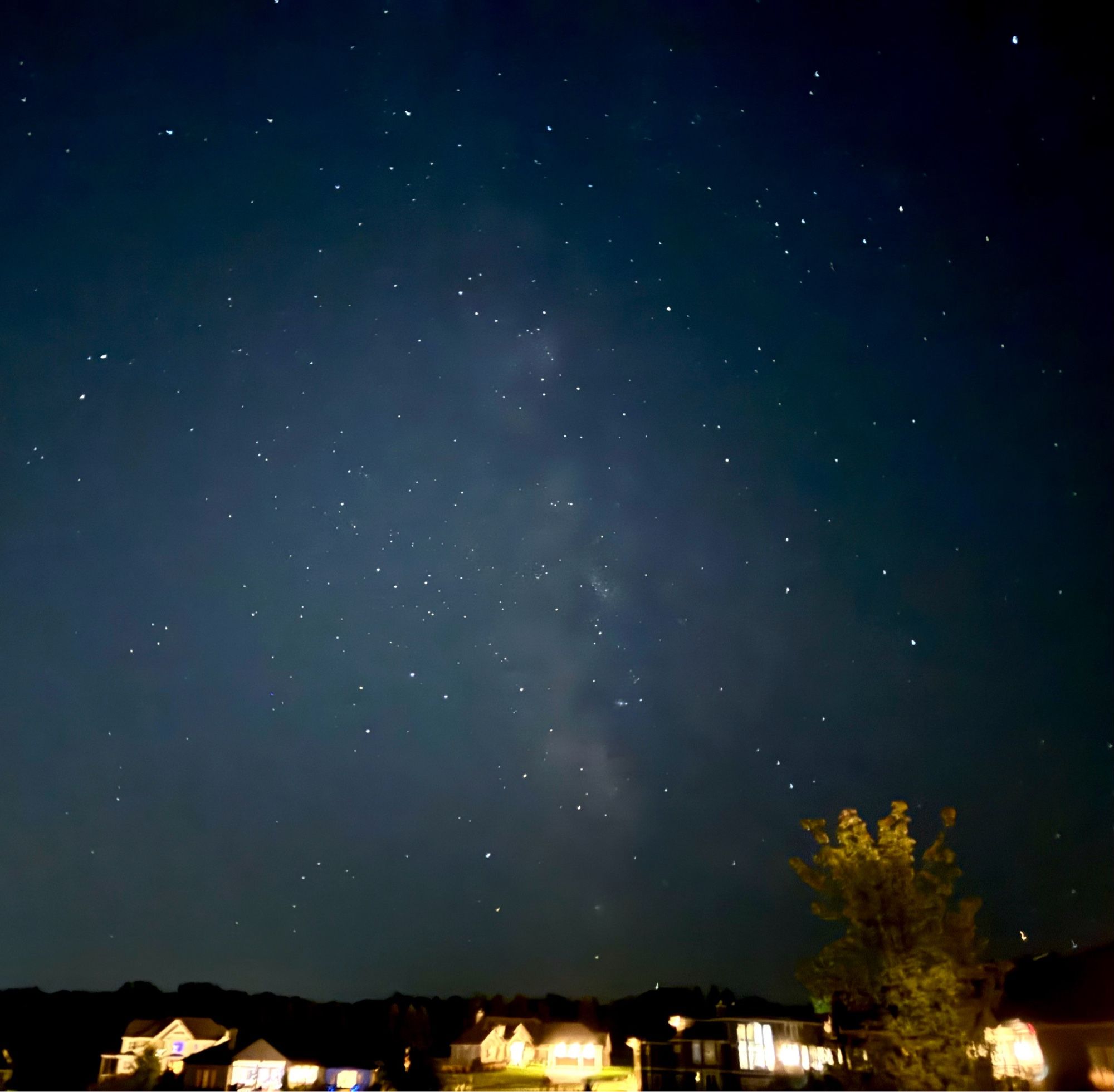 Overly lit houses with a dark starry sky above and the Milky Way standing on end.