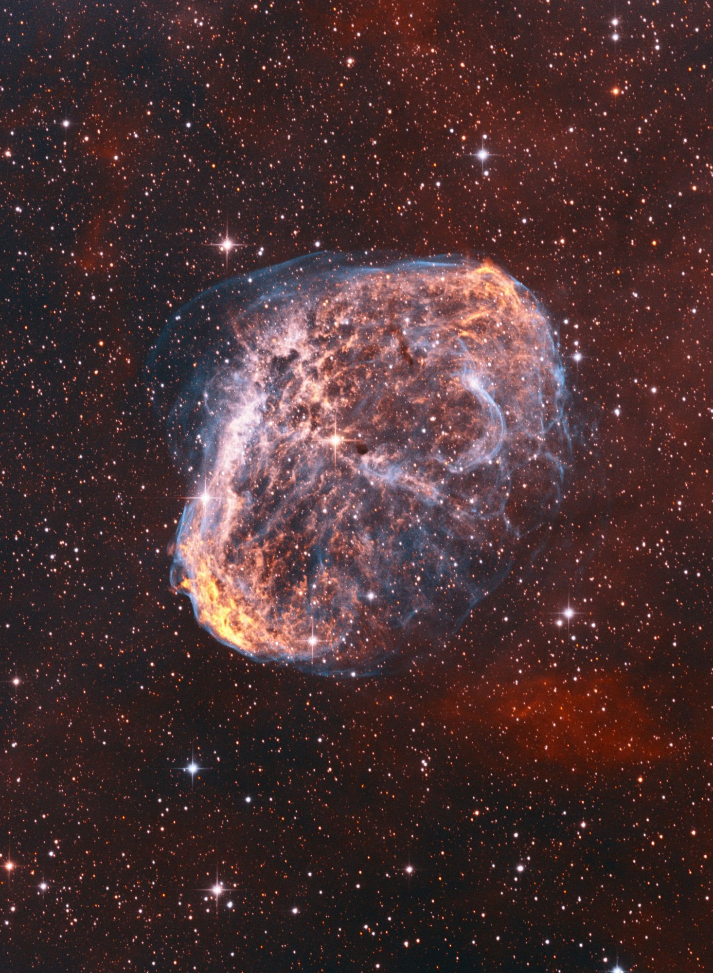 "A striking image of NGC 6888, known as the Crescent Nebula, set against a rich star-filled backdrop. The nebula, located in the constellation Cygnus, appears as a delicate, glowing arc of gas, with vivid hues of orange and blue highlighting its intricate structure. The wispy outer edges of the nebula extend into the surrounding space, creating a dynamic, almost ethereal appearance. This nebula, formed by powerful stellar winds from its central star, stands out beautifully amidst the surrounding stars, each twinkling with varying intensity and color."