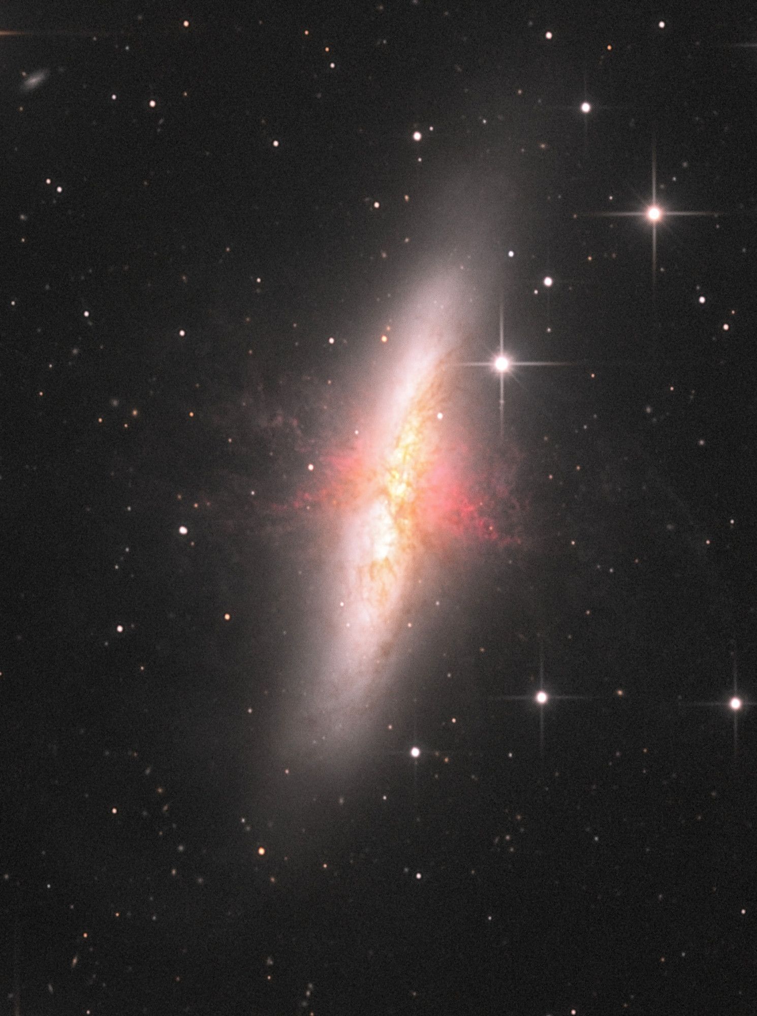 "An intense and captivating image of Messier 82, commonly known as the Cigar Galaxy, located approximately 12 million light-years away in the constellation Ursa Major. The galaxy is seen edge-on, with a bright, elongated core emitting a striking burst of red and orange hues, indicative of vigorous star formation. The surrounding space is dotted with stars, but the galaxy itself commands attention with its dramatic, almost fiery appearance, a hallmark of its classification as a starburst galaxy. The contrast between the glowing core and the darker outer regions highlights the dynamic activity within this remarkable celestial object."