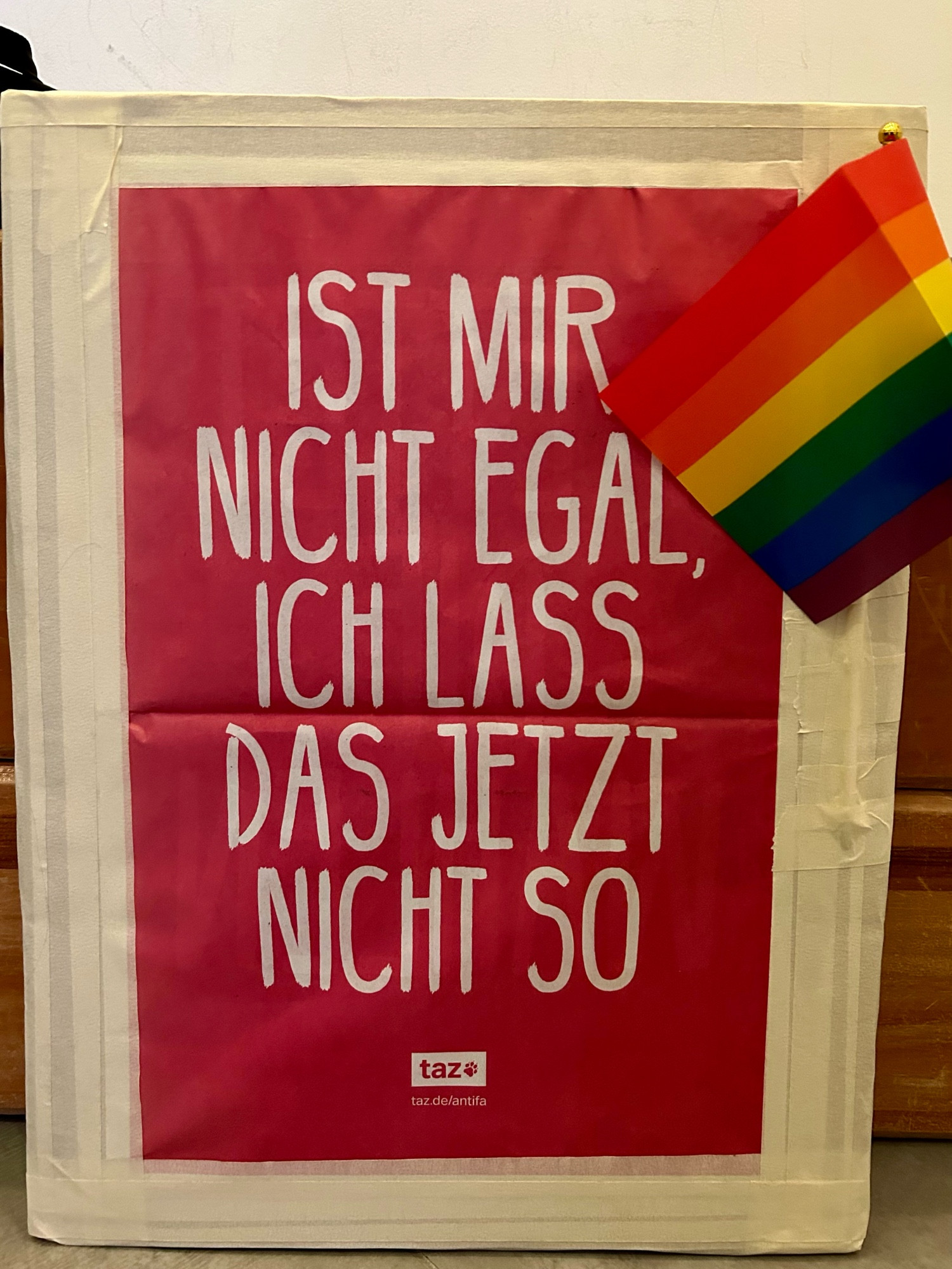 Plakat: Ist mir nicht egal, ich lass das jetzt nicht so. Daran angeklebt eine Regenbogenfahne.