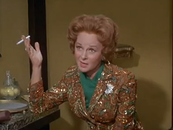 Susan Hayward as Helen Lawson in The Valley of the Dolls, smoking a cigarette, in a gold pantsuit and green scarf