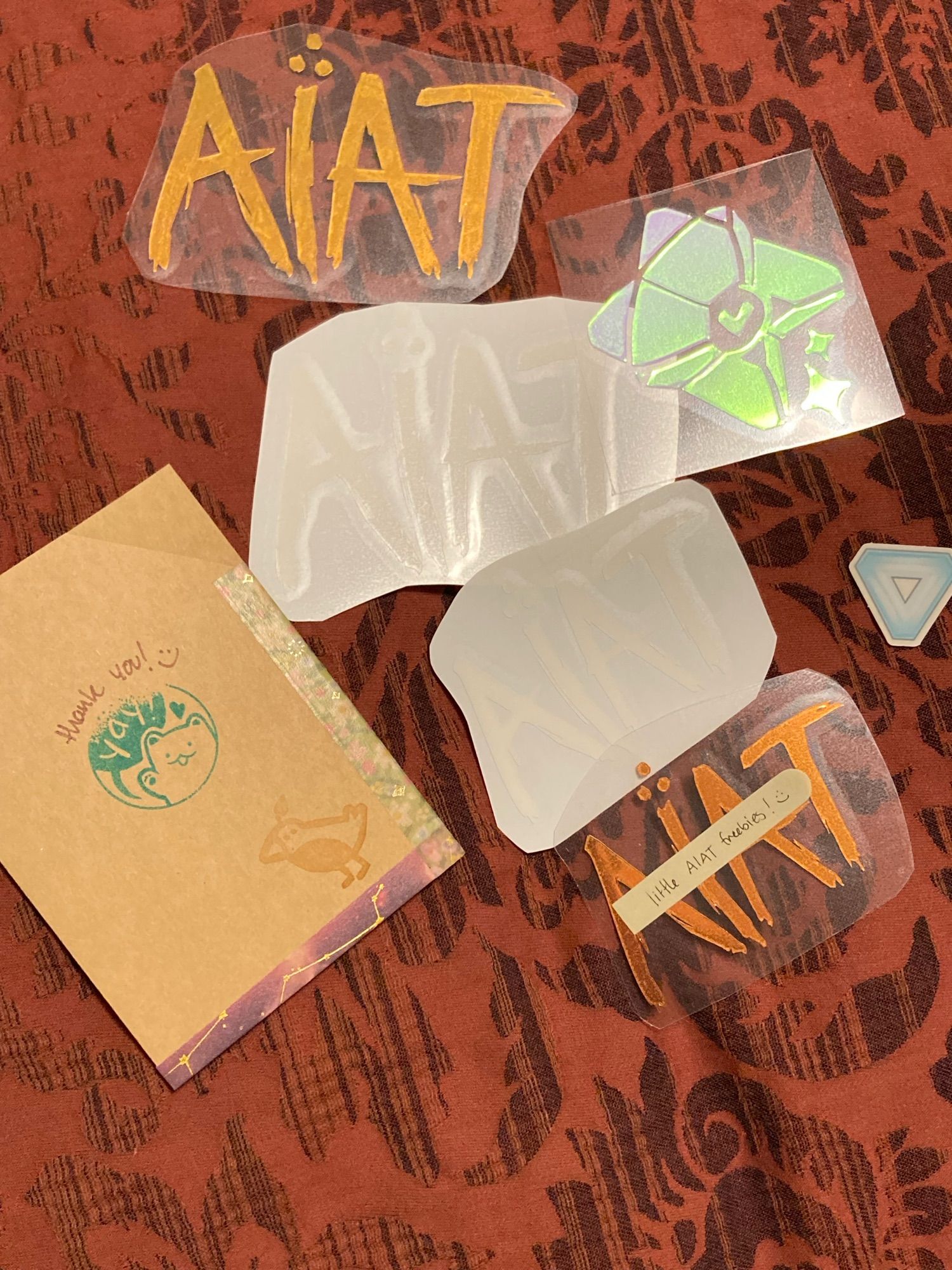 Two copper iridescent colored and two glow in the dark ‘AIAT’ decals, and one rainbow iridescent ghost from Destiny decal, and a small note from Destiny sticker.