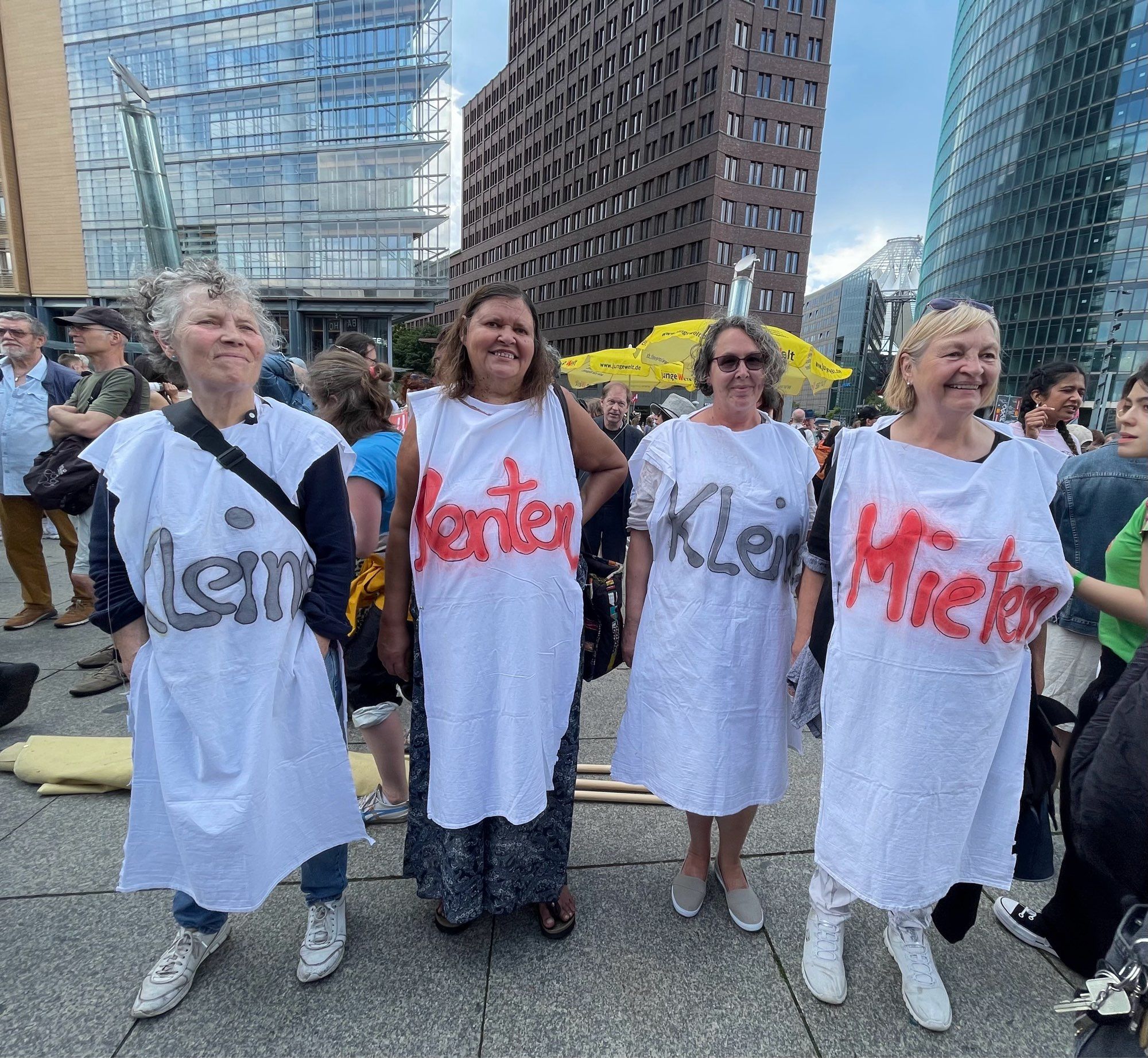 Vier ältere Frauen in weißen Kleidern. Von links nach rechts steht vorne auf den Kleidern geschrieben „Kleine“ „Renten“ #Kleine“ „Mieten“