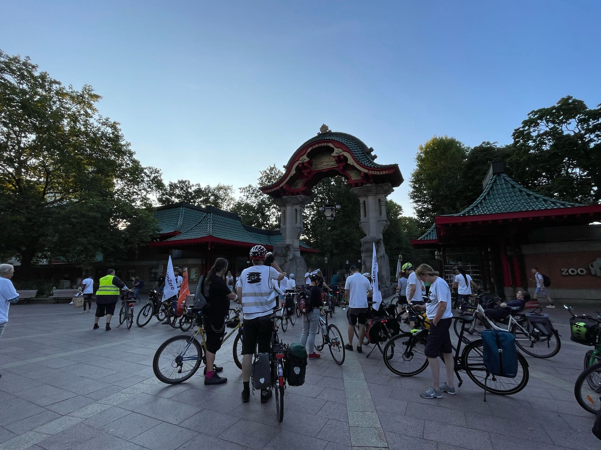 Radfahrende, einige tragen ein weißes T-Shirt, stehen vor dem Elefantentor des Berliner Zoos.