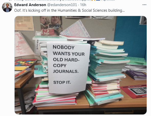 A pile of old paper journals with a sign on them saying "nobody wants your old hard copy journals. Stop it."