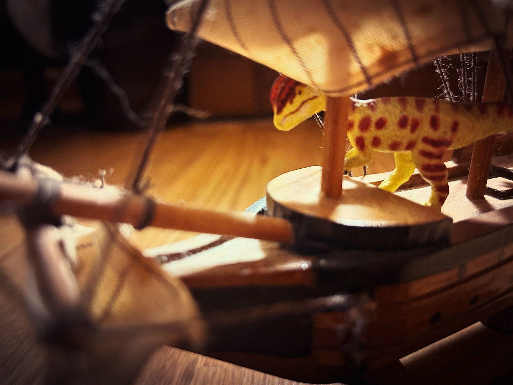 A green Dilophosaurus with brown spots riding a small and dusty model pirate ship.