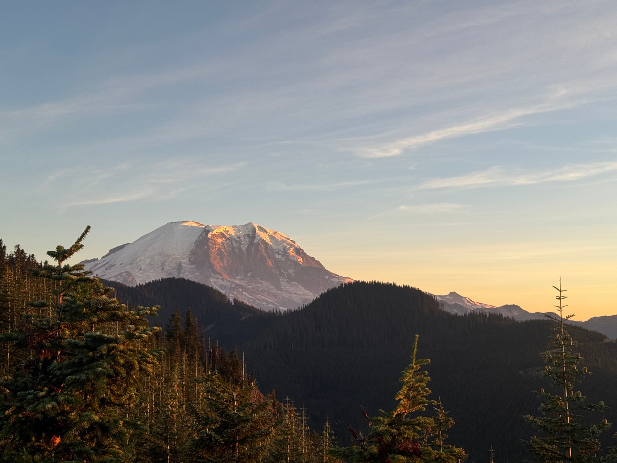 A photo of Mt. Rainier at sunset with tree covered hills on the foreground 