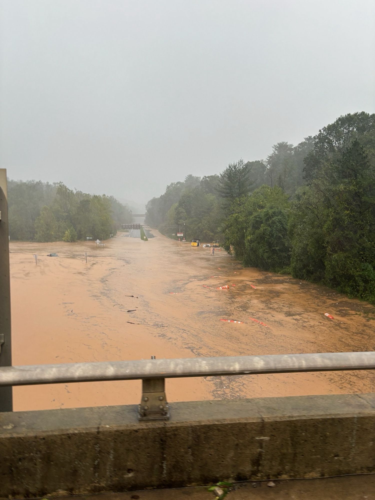 A flooded highway that looks like a river. Original message:

⬇️ You're standing on I-40, looking down at U.S. 74.
❗ The Blue Ridge Parkway bridge is in the distance.
⚠️ Don't go out today. It's not safe.
#Helene #ncwx