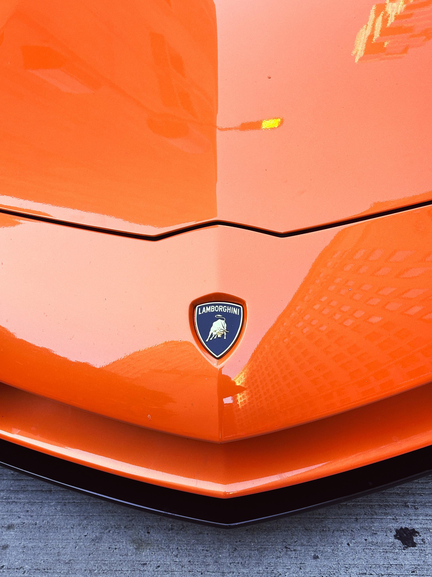 The hood of an orange Lamborghini in Manhattan. The hood is shiny and is reflecting buildings. 