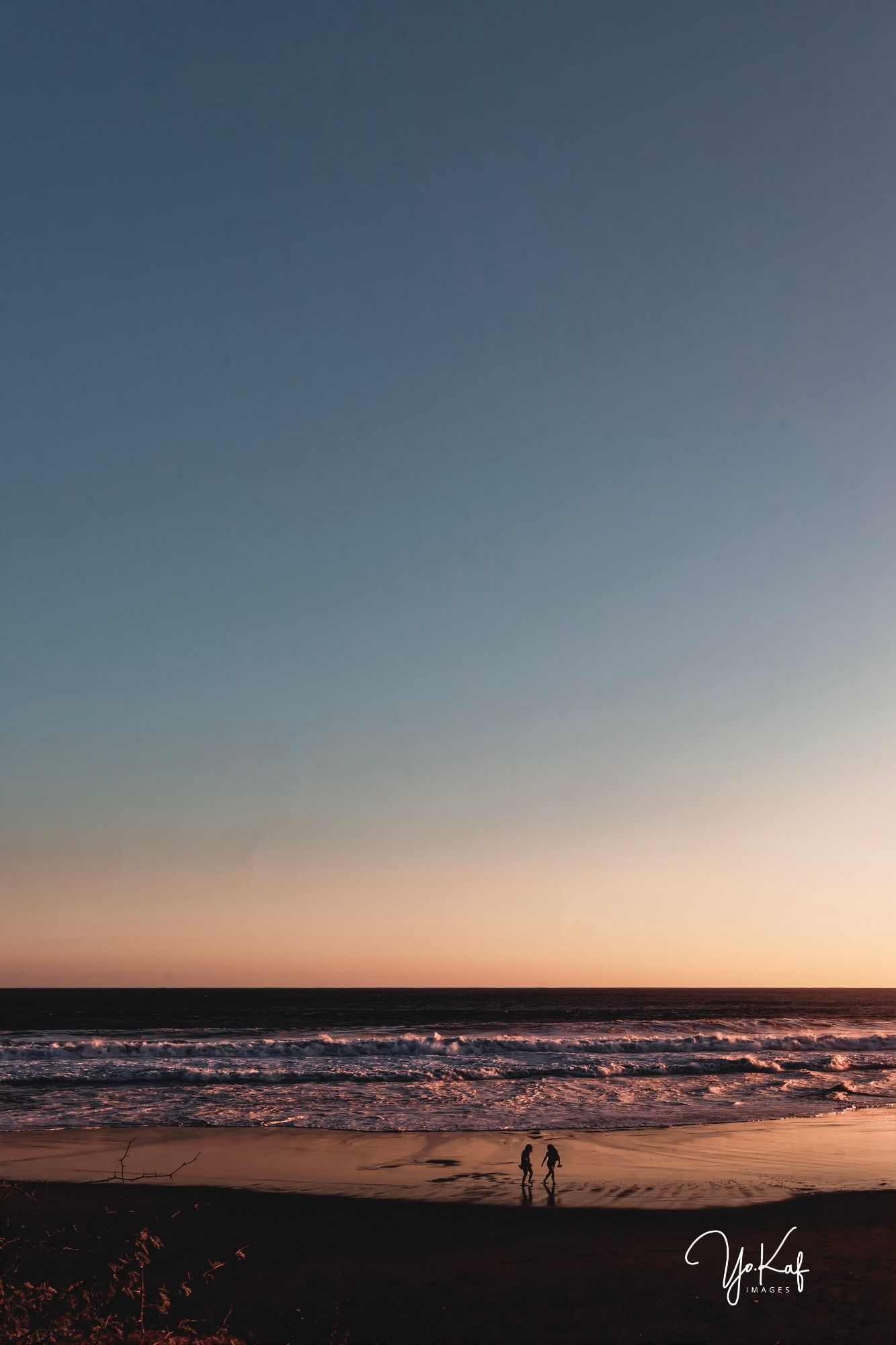 A minimalist picture of beach with 2 personn on a black sand beach