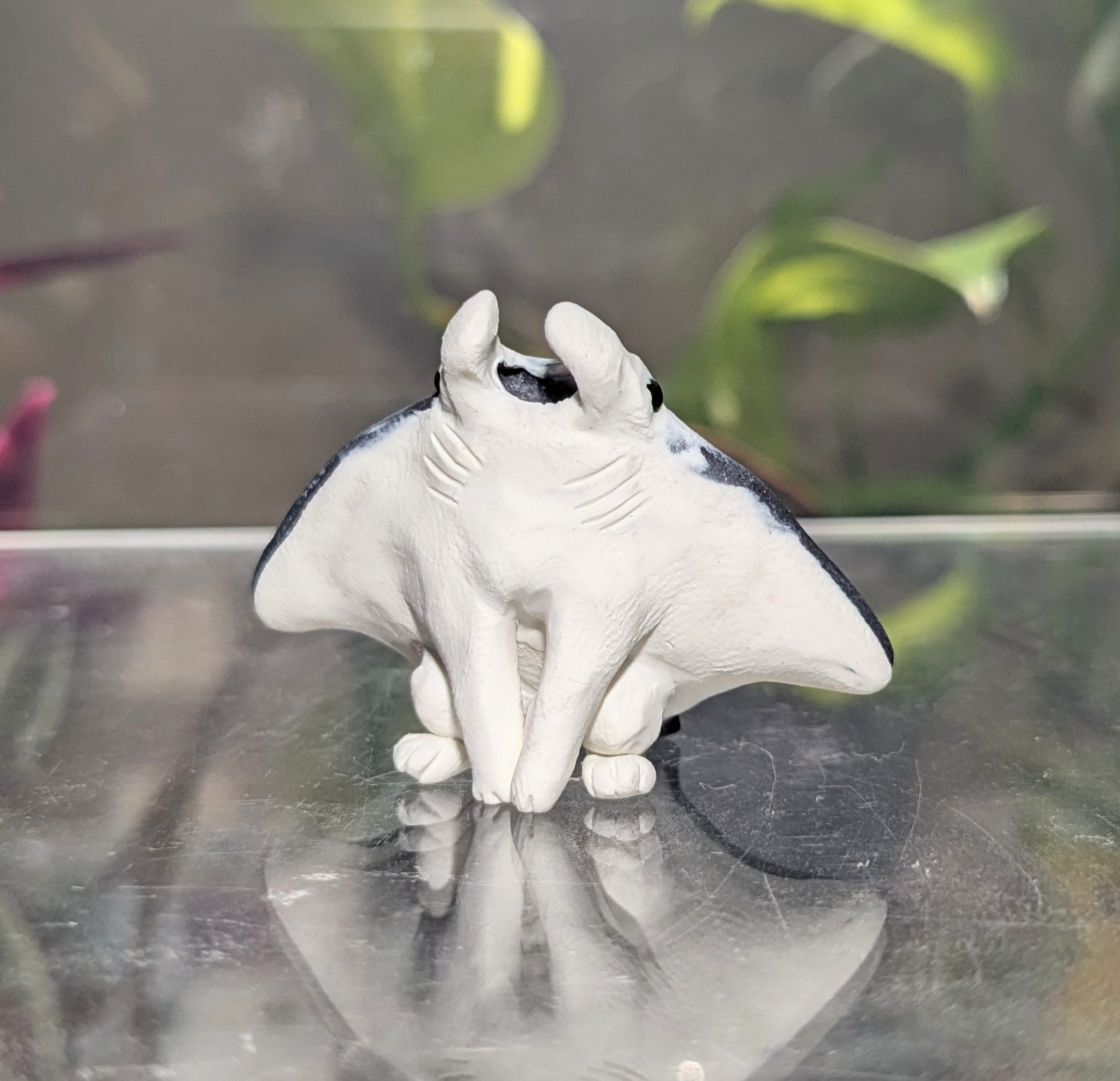 A figurine of a Manta Ray-like creature. It resembles a manta with stubby little legs, and is seated, facing the viewer with a big smile. As she is a ray, from the front, it is her white underside that's visible.