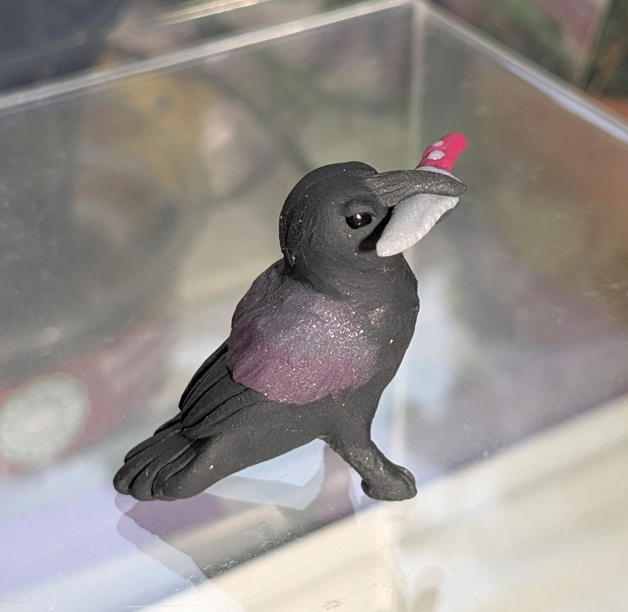 A figurine of a crow, holding a knife in his beak. His face is tilted up, and he looks full of glee and ill intent.