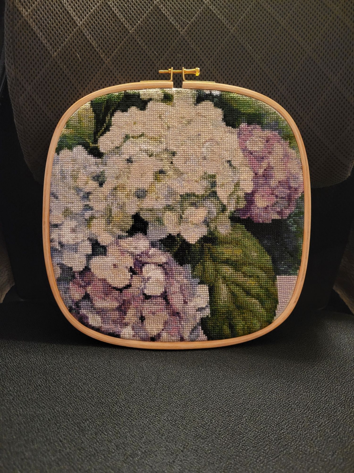 A 10" rounded square hoop with a finished cross-stitch project depicting clusters of white, purple, and blue hydrangeas surrounded by green leaves.