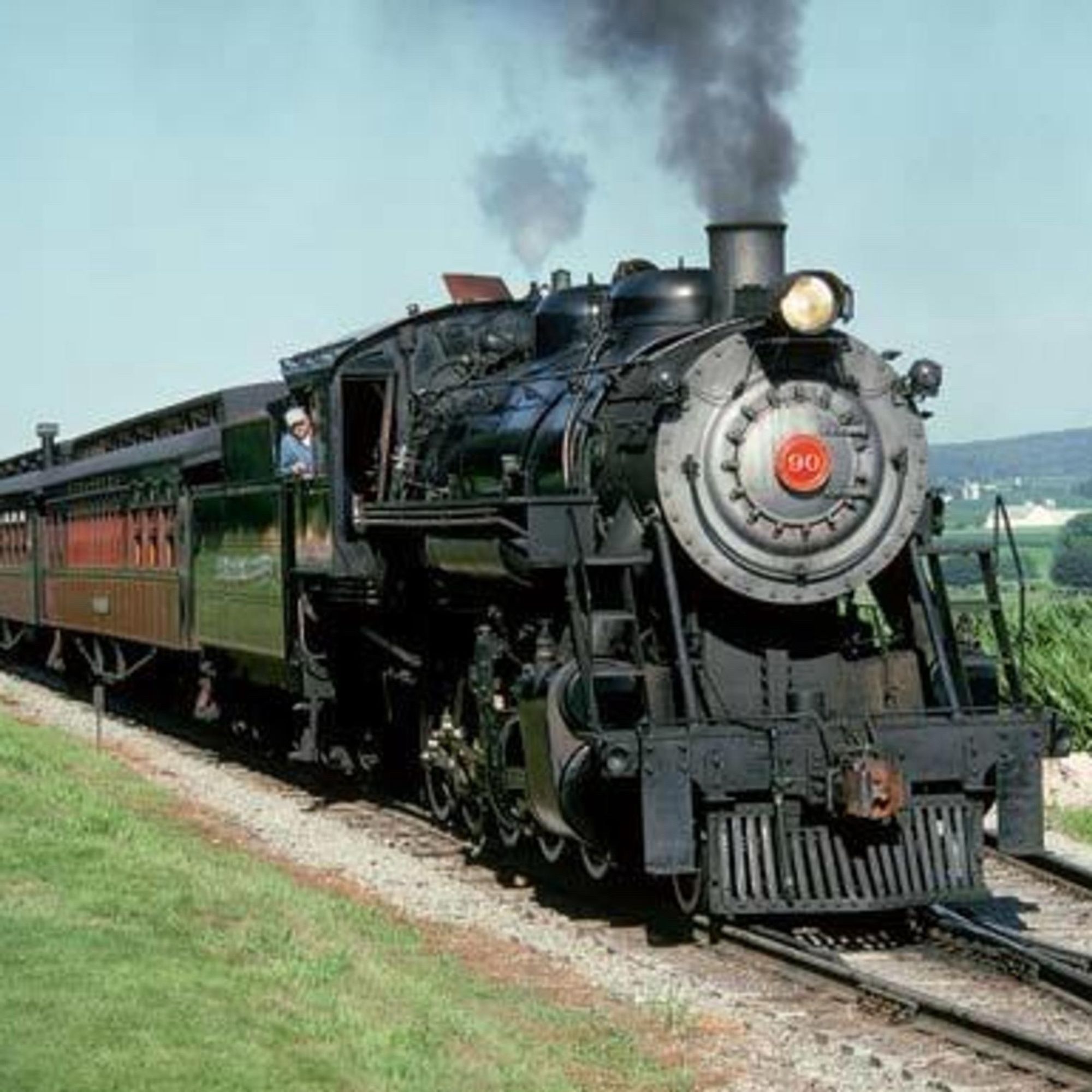 Steam engine pulling red passenger coaches through the countryside