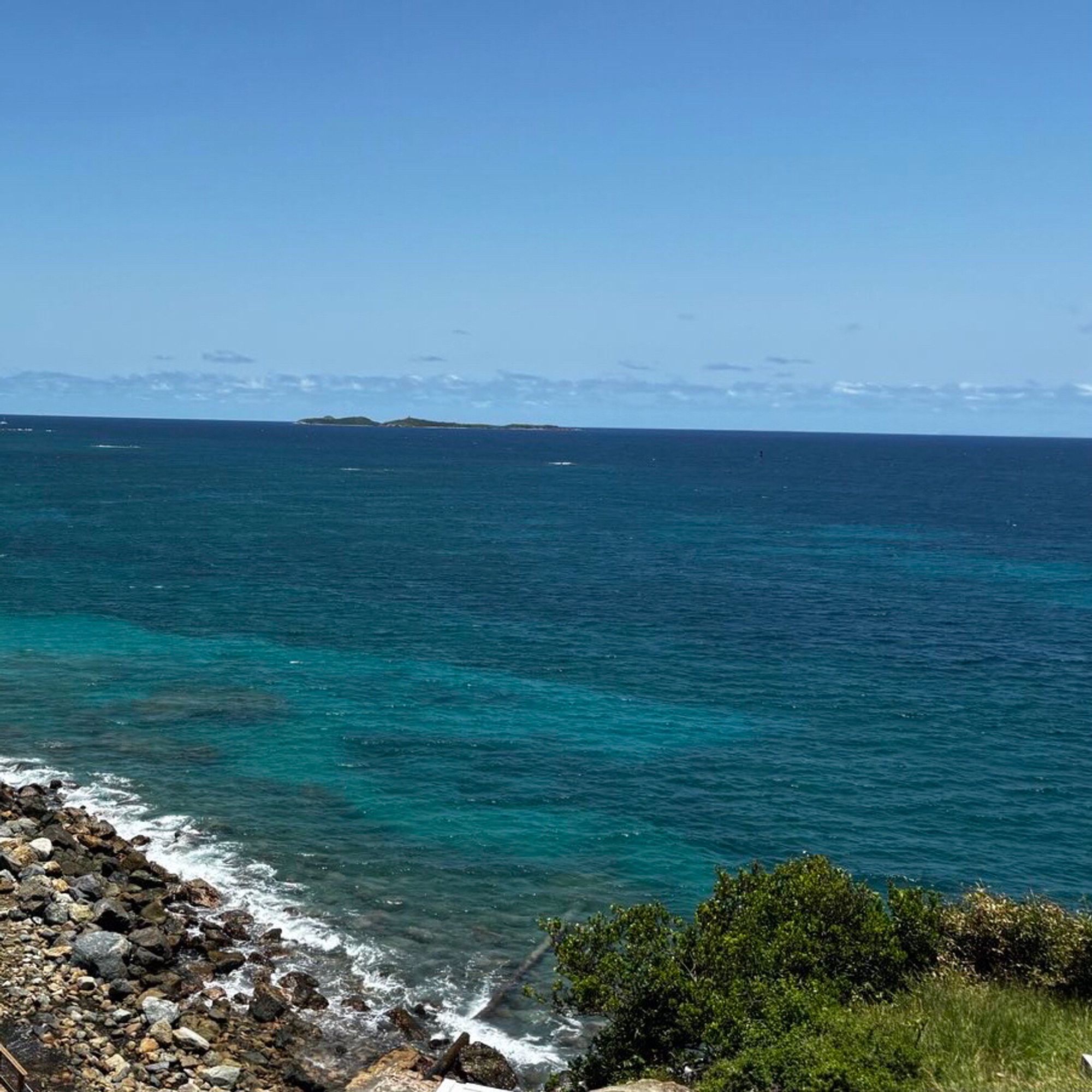 Seascape. Rocky shore with crystal green/blue water. Island in far distance. Bushes in the foreground. Taken in the Caribbean.