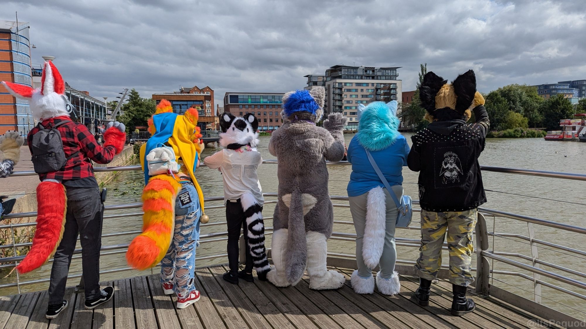 A group of fursuiters looking out over a wharf on a cloudy day. Their backs are to the camera.