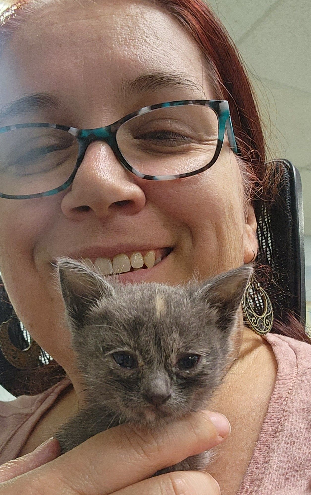 Sept '23. Teeny tiny grey kitten held under my chin as I smile broadly. She looks like a grey cotton ball with ears and a blaze of peach in the middle of her forehead.