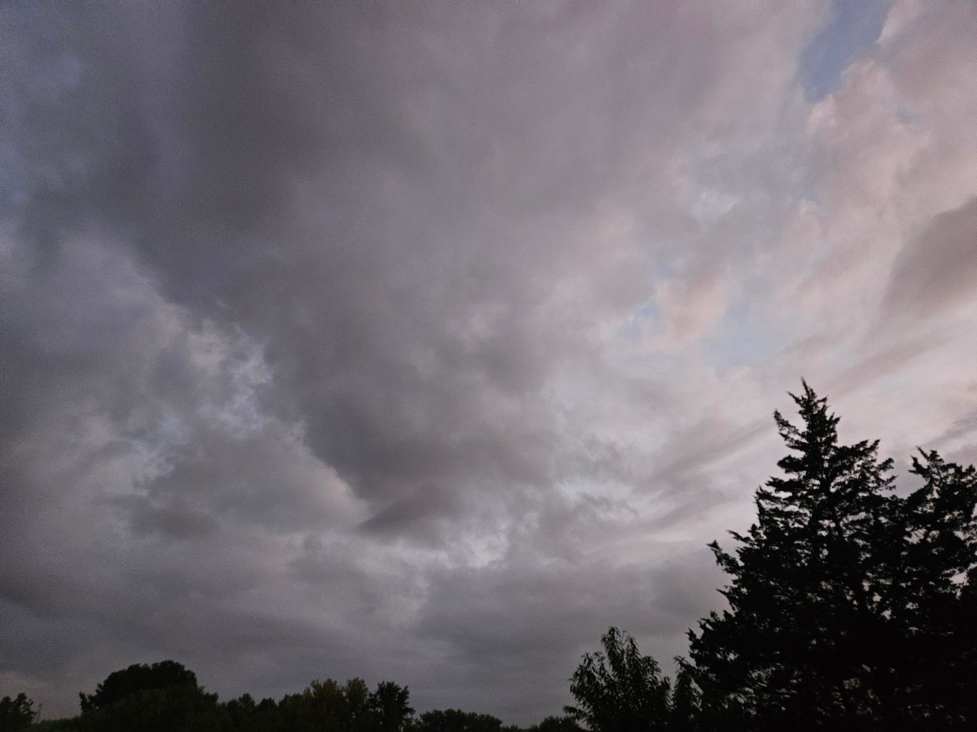 Fluffy gray morning clouds hiding hints of a pale blue sky. The silhouettes of trees frame the bottom.