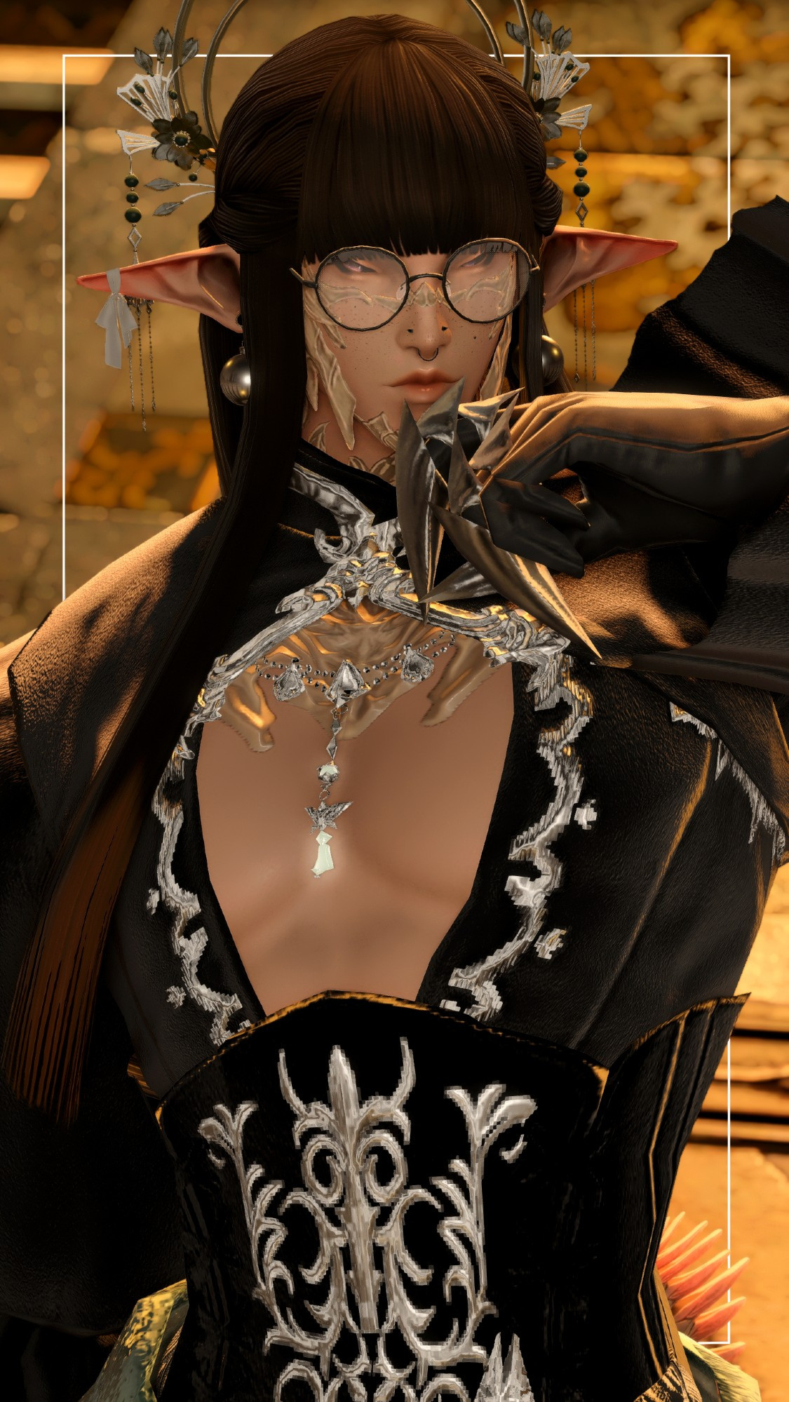 A male Raen Au Ra wearing a gothic top with a black and silver corset, silver accents up to the collar. He wears a silver headpiece with flowers and two hoops, one bigger than the other. He has elf ears with globe earrings, one earring with a bandage at the tip of the ear. Faint purple eyes with golden hues in them, halfway closed. He also wears black rimmed circular glasses. Long, straight hair with blunt bangs. Gloves with two silver claws at the index and middle finger.