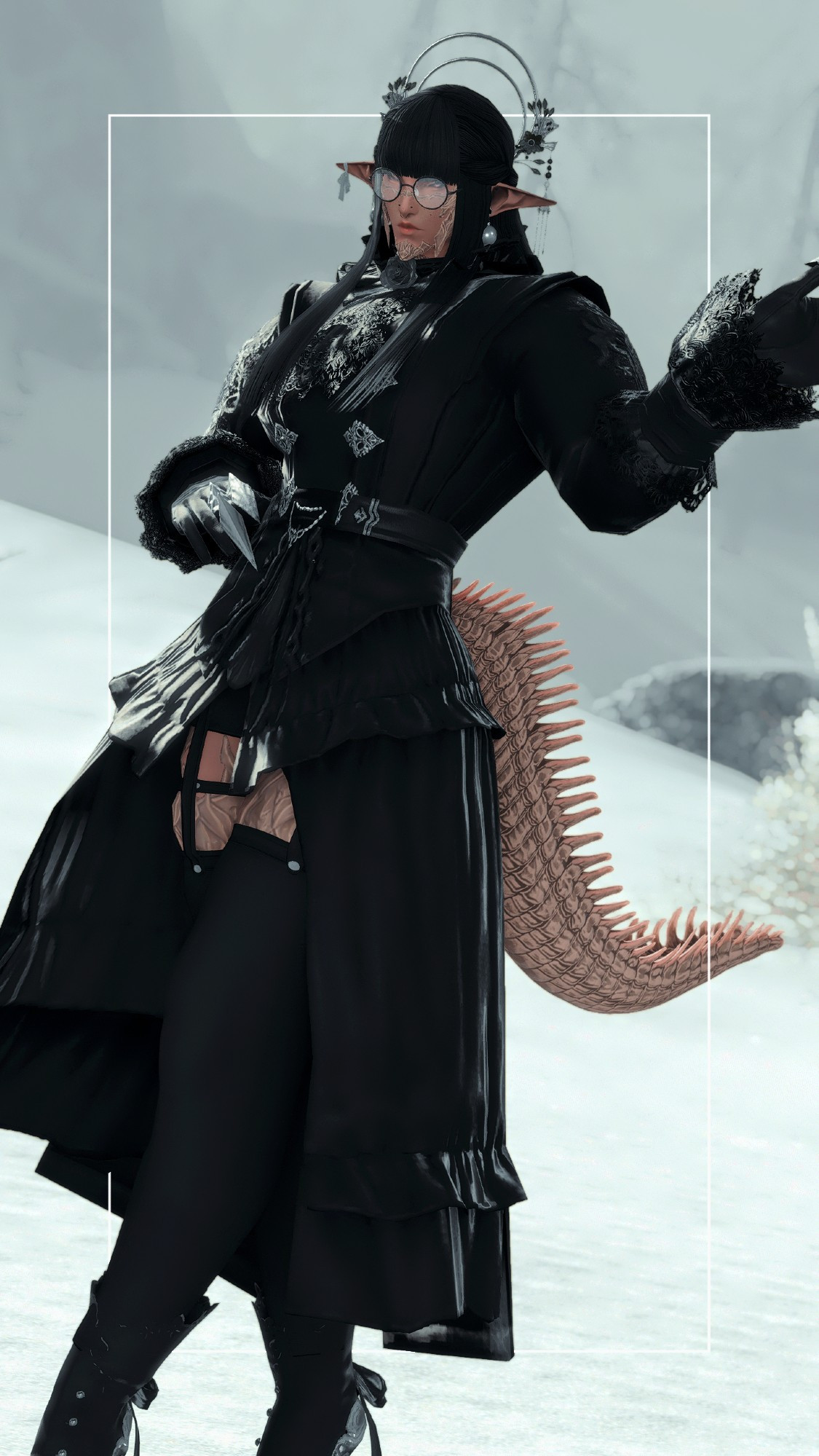 A male Raen Au Ra wearing a gothic top with a skirt attached to it, open towards the front. He wears black rounded glasses as well. Black top, with subtle forest green lace details, silver clasps and chains. The Au Ra also has elf ears with globe earrings and a bandage attached at the tip of the ear for one. The man wears black gloves with two silver claws attached. A cream/ivory crocodile's tail, as well as black opaque stockings with a harness attached to matching black shorts underneath and black boots with a forest green bow on the back. Long, black hair with blunt bangs with an ornate floral headpiece with two hoops on the back.