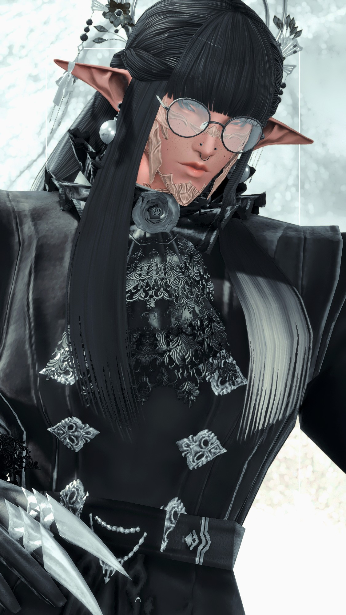 A male Raen Au Ra wearing a gothic top with a skirt attached to it, open towards the front. He wears black rounded glasses as well. Black top, with subtle forest green lace details, silver clasps and chains. The Au Ra also has elf ears with globe earrings and a bandage attached at the tip of the ear for one. Long, black hair with blunt bangs with an ornate floral headpiece with two hoops on the back.