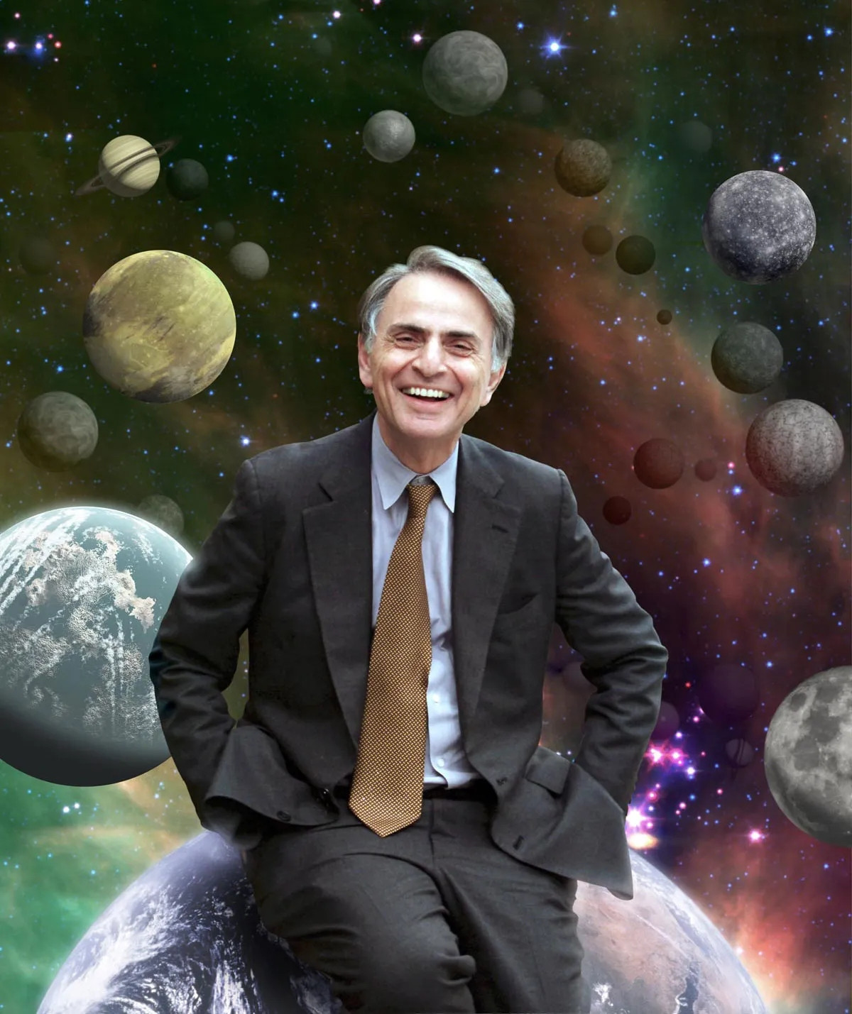 A smiling gray-haired Carl Sagan is sitting in front of a backdrop depicting lots of planets of varying sizes and colors. He is wearing a dark gray suit with a light blue shirt and brown tie.