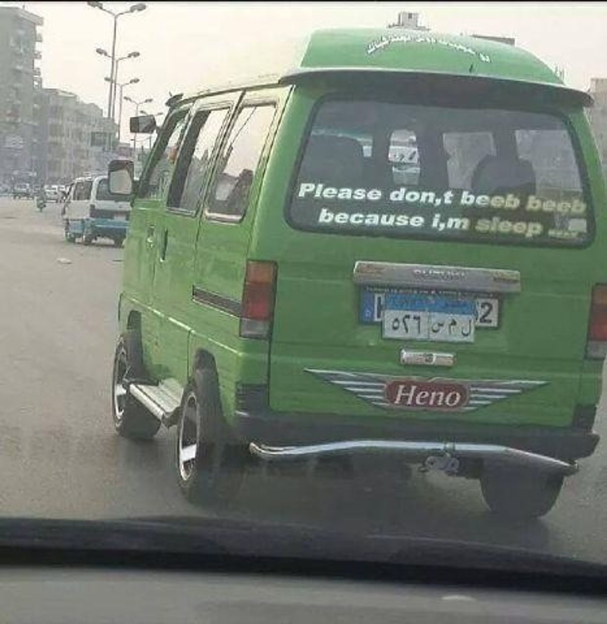 a lime green Heno minivan on the road with a decal on the rear glass reading "Please don,t beeb beeb because i,m sleep ...."