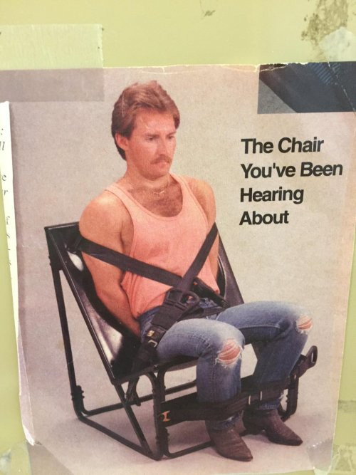 an image of "the chair you've been hearing about," which a man is strapped into w/two across-the-chest belts and a foot restraint