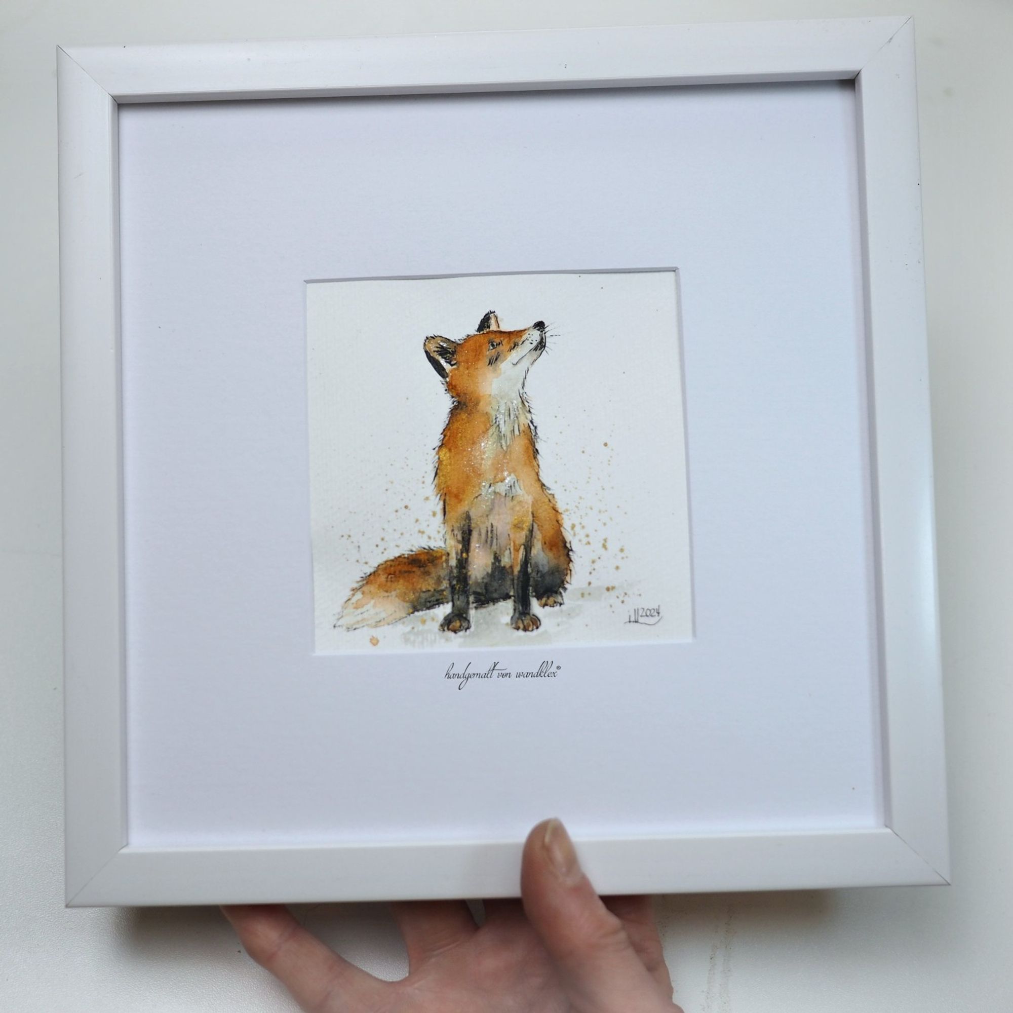 auf 20x20cm gerahmtes kleines Aquarell: sitzender Fuchs der skeptisch nach rechts oben schaut. Halte das Bild mit einer Hand in die Kamera, auch damit man die Größe einschätzen kann