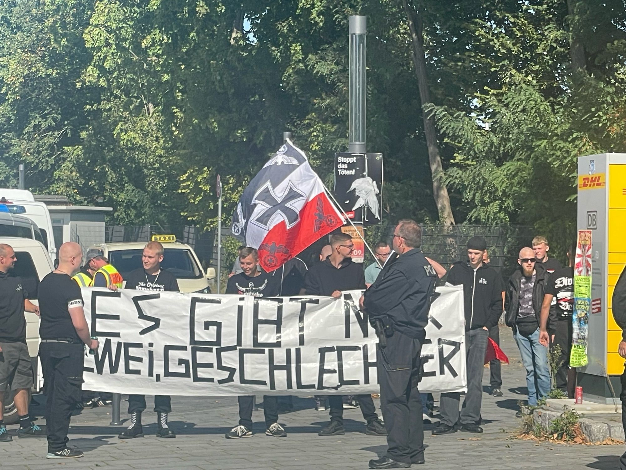 Bild von den Nazis am Bahnhof mit Transpi „Es gibt nur zwei Geschlechter“ und anderer Fahne.