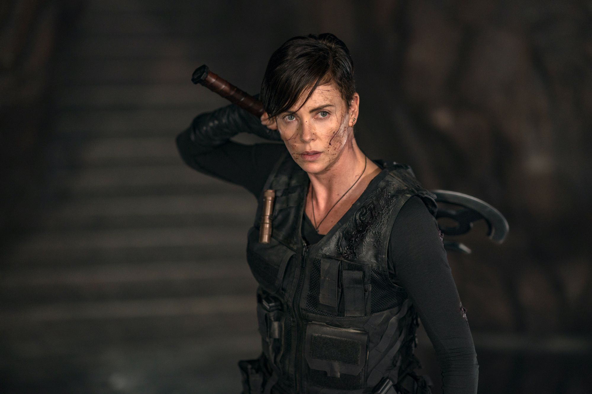 Andi, with short hair and dirt on her face, wearing modern combat armour but also wielding a double-bladed battle axe.