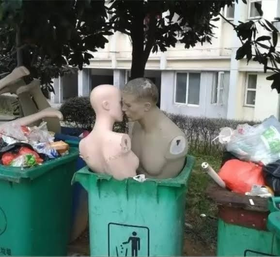 dois manequins posicionados dentro de uma lixeira como se estivessem se beijando 