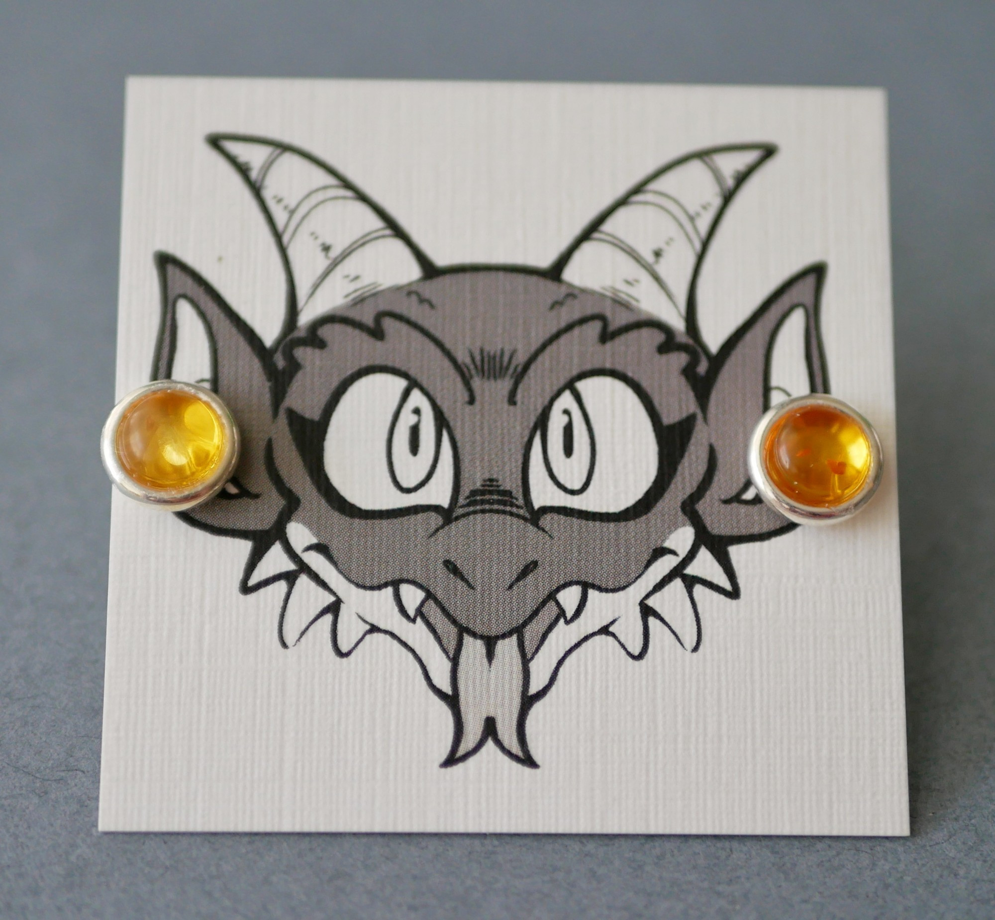 amber earrings on an earring card with Bauble the kobold on it looking like he's wearing the earrings