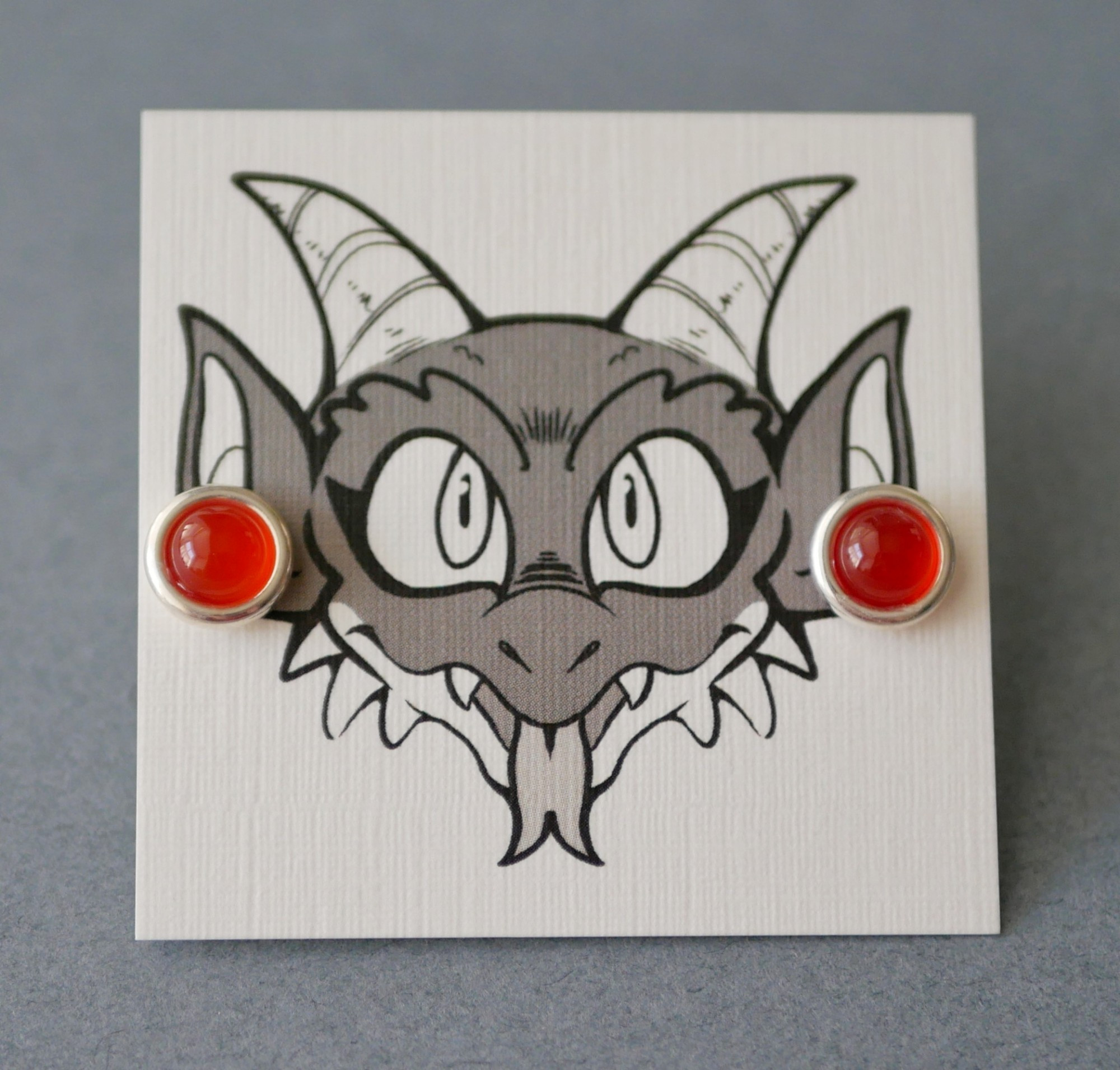 carnelian earrings on an earring card with Bauble the kobold on it looking like he's wearing the earrings