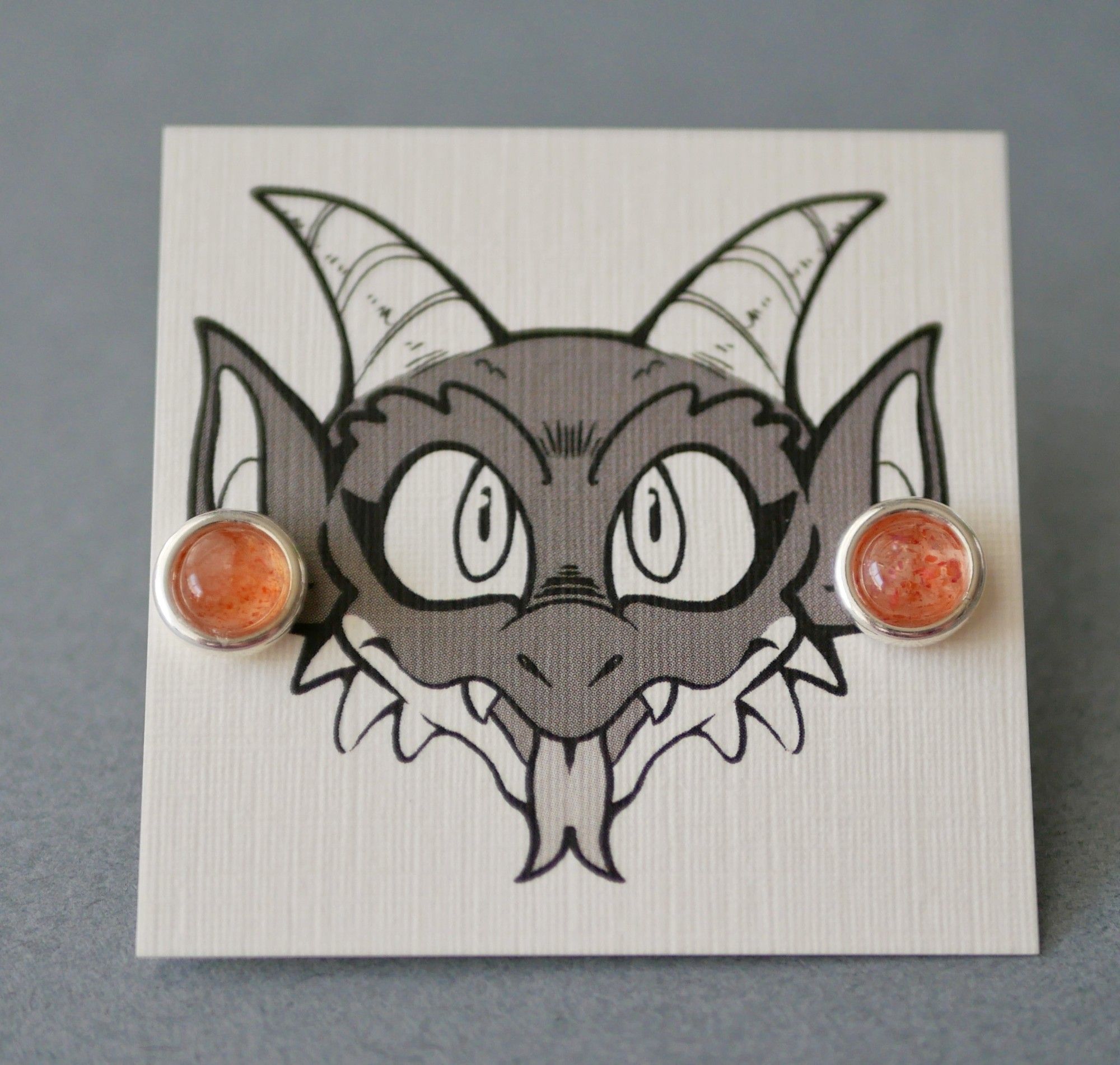 sunstone earrings on an earring card with Bauble the kobold on it looking like he's wearing the earrings