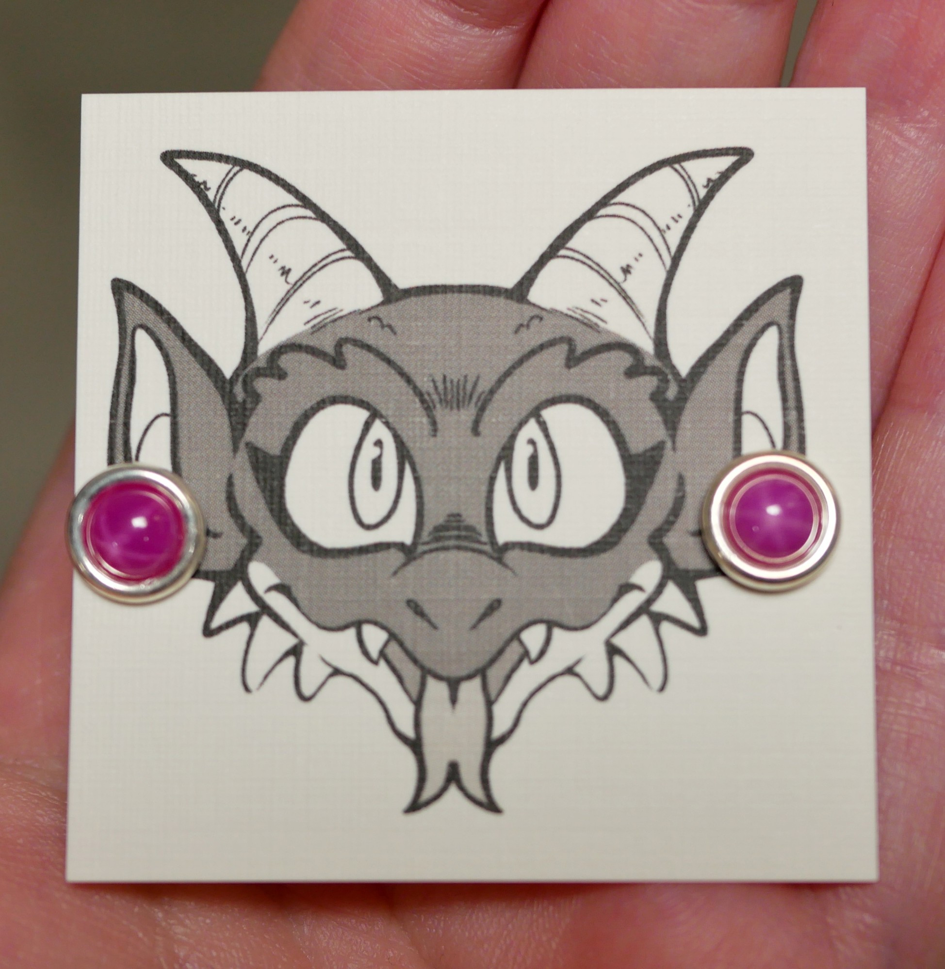 star ruby earrings on an earring card with Bauble the kobold on it looking like he's wearing the earrings