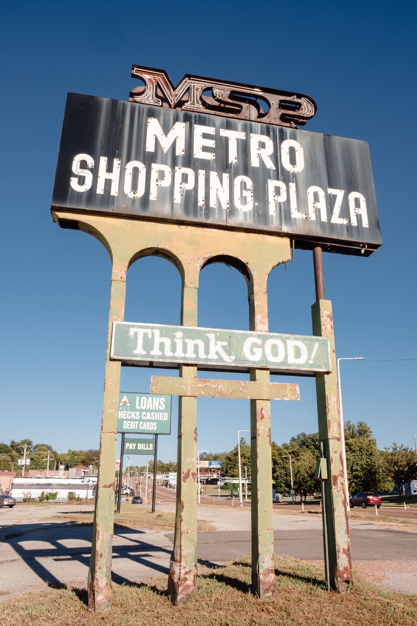 Sign for the dilapidated Metro Shopping Plaza with its reminder to “Think God.”