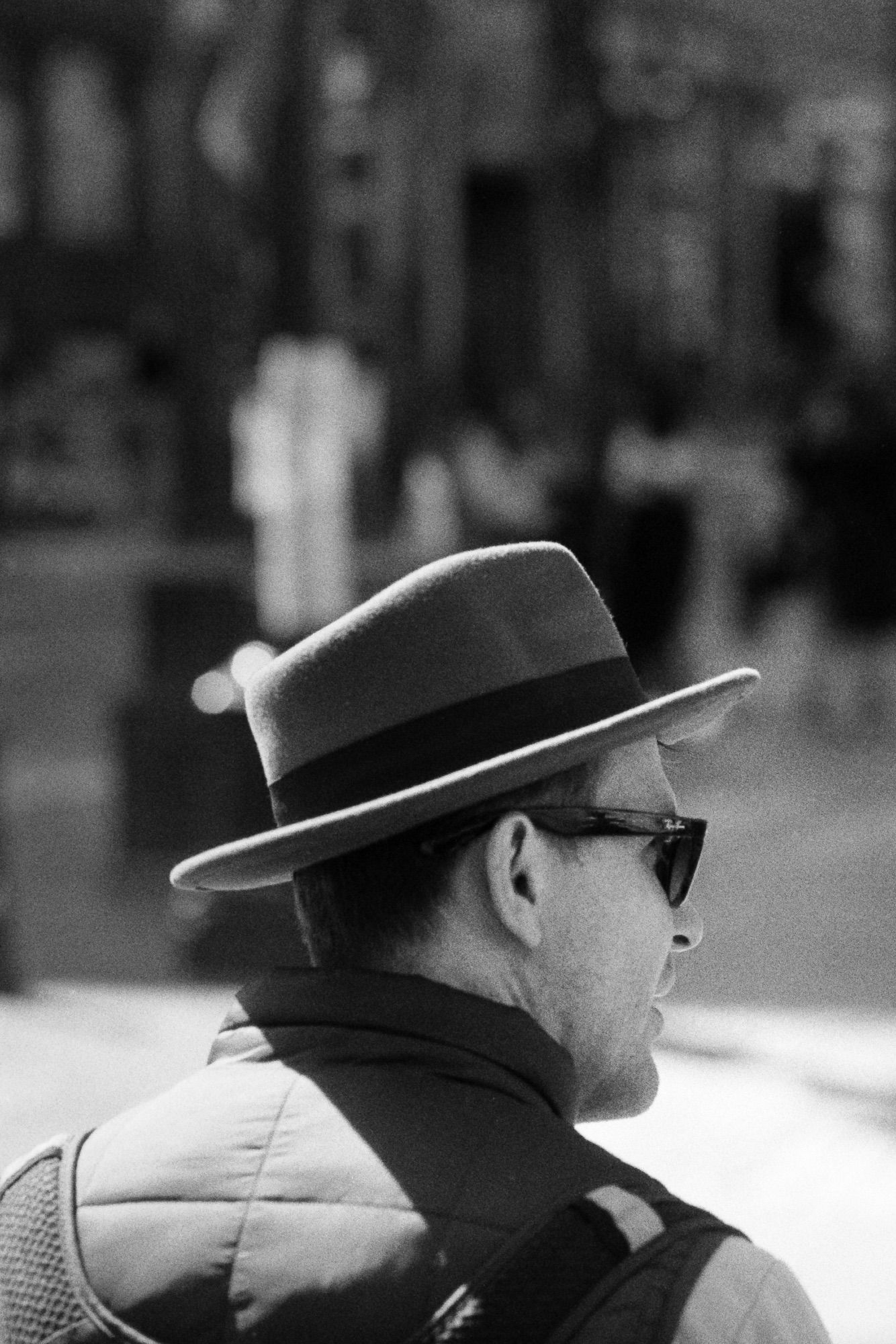 A man in a hat and sun glasses listens to a companion out of the frame.