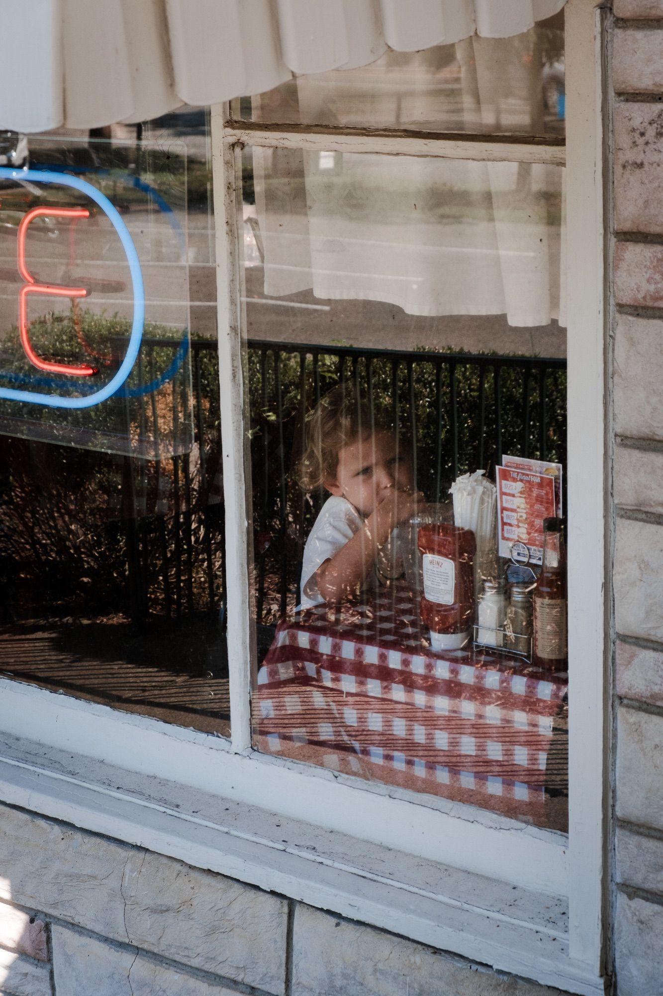 A child visible through a cafe window tucks into her breakfast.