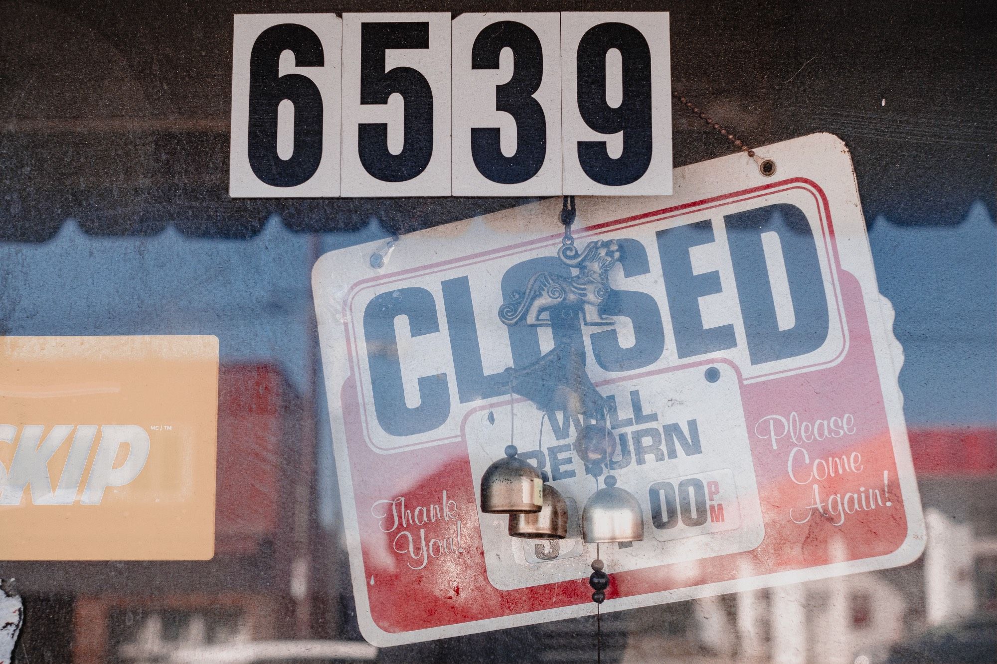 A sign declares that a store is closed. The “will return” portion of the sign is obscured by trinkets and bells.