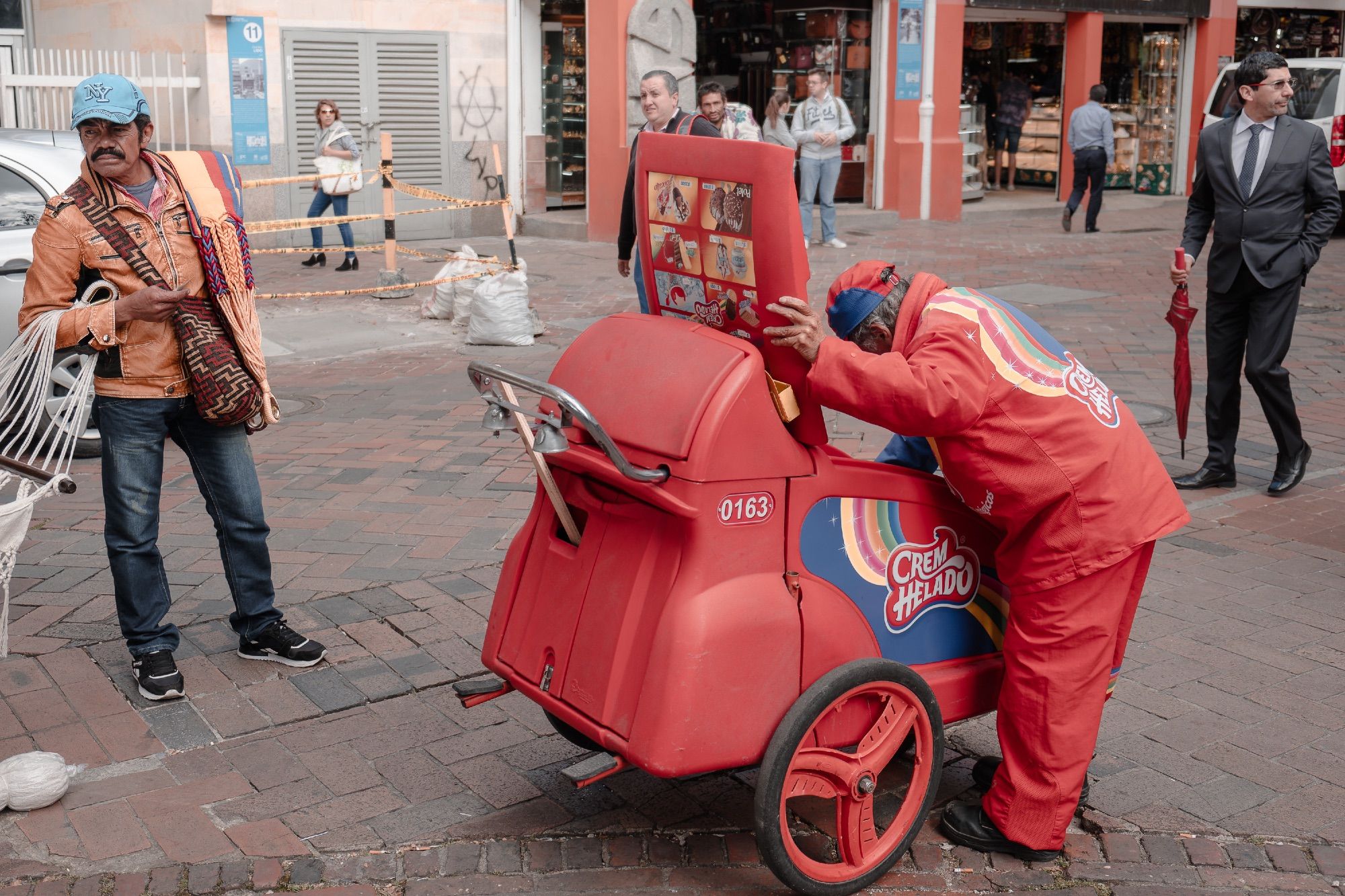 A hammock vendor, an ice cream man, and a businessman share the street.