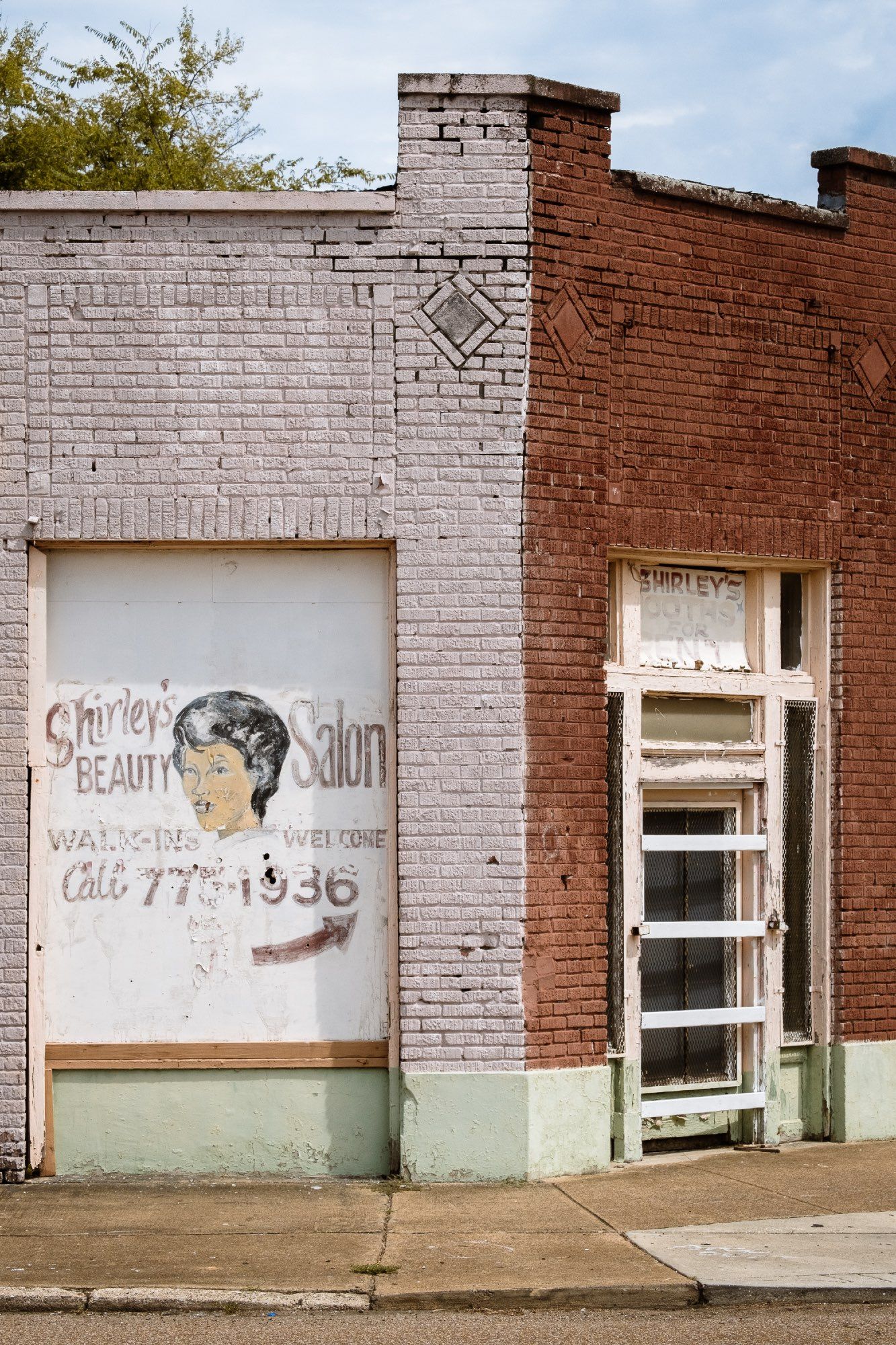 A hand painted sign for Shirley’s Beauty Salon is affixed to the side of a tired but colourful building.