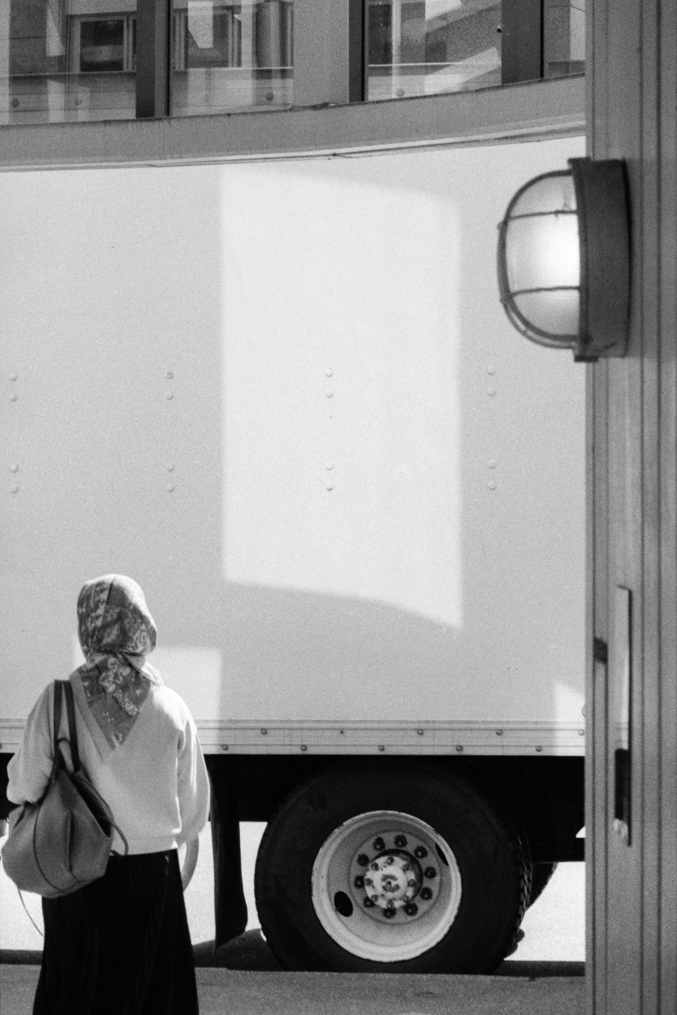 A woman waits on the sidewalk as light splashes across a tractor trailer.